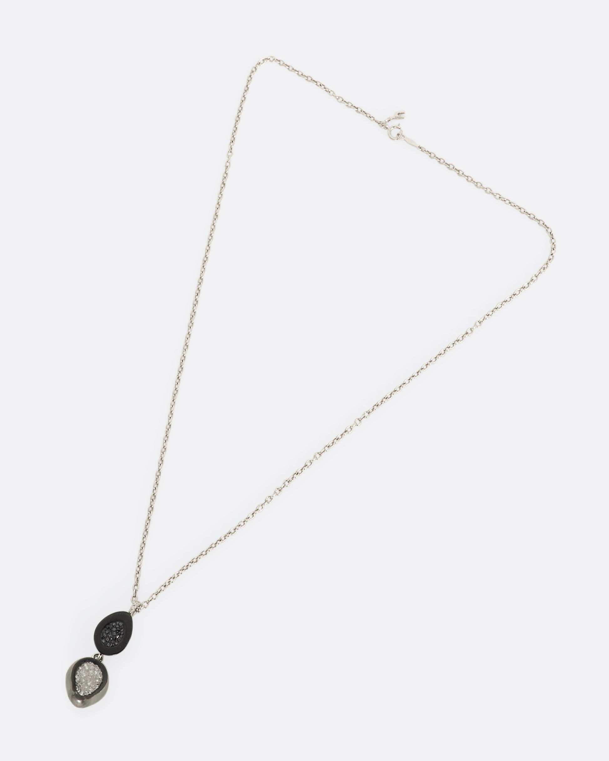 A white gold necklace with a double tiered Tahitian pearl pendant lined with black and white diamonds and a pave diamond bail. View laying flat of entire necklace.