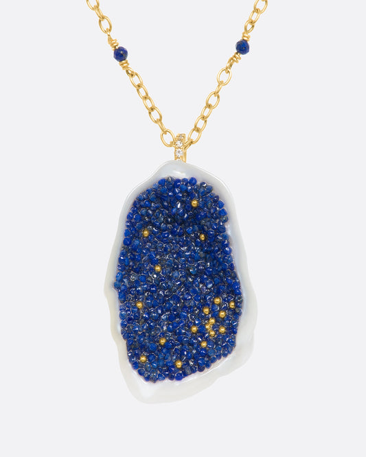 A yellow gold necklace with a hollowed out pearl pendant filled with lapis and 22k gold beads. Shown from the front.