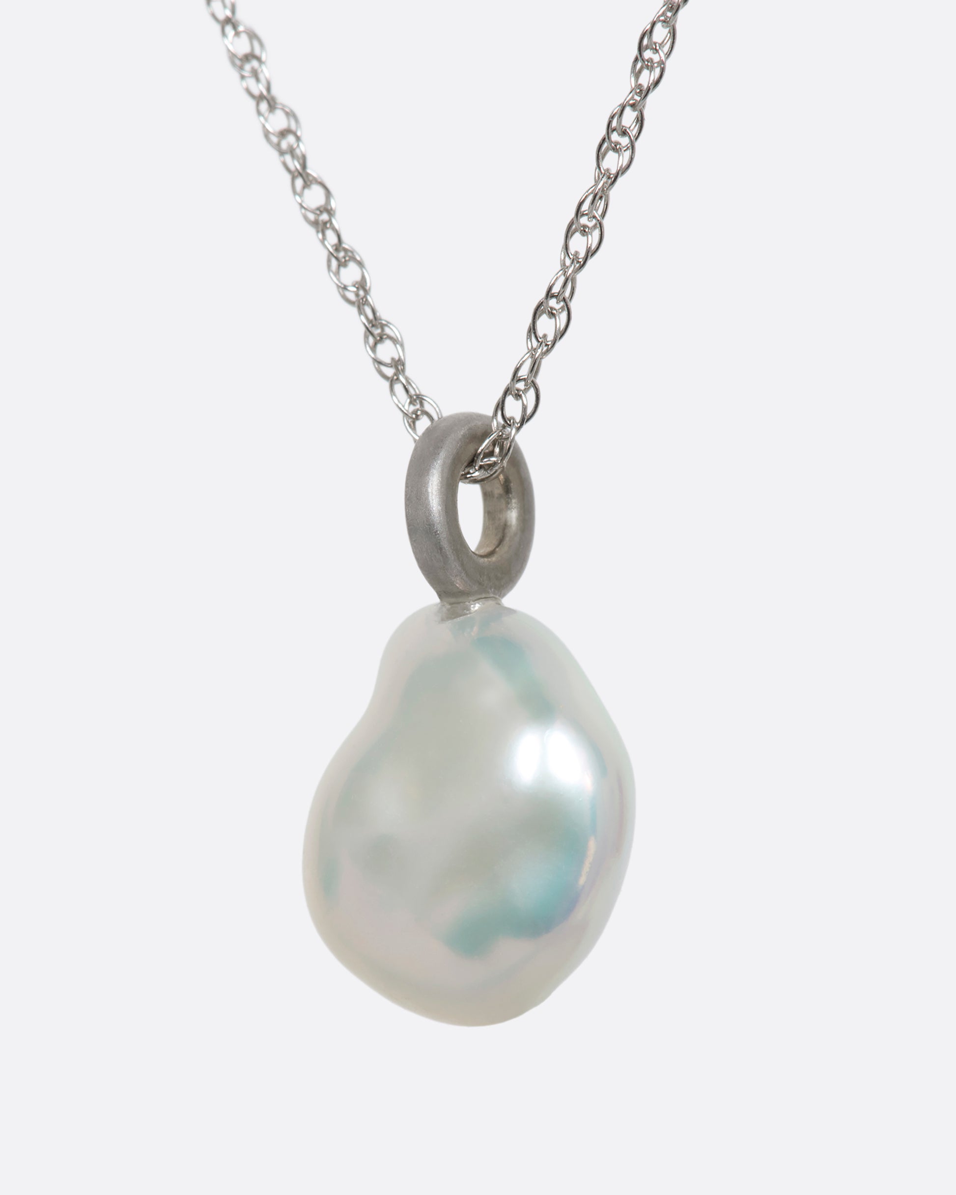 A white keshi pearl pendant filled with reclaimed sapphires hanging on a white gold chain. View from the back.