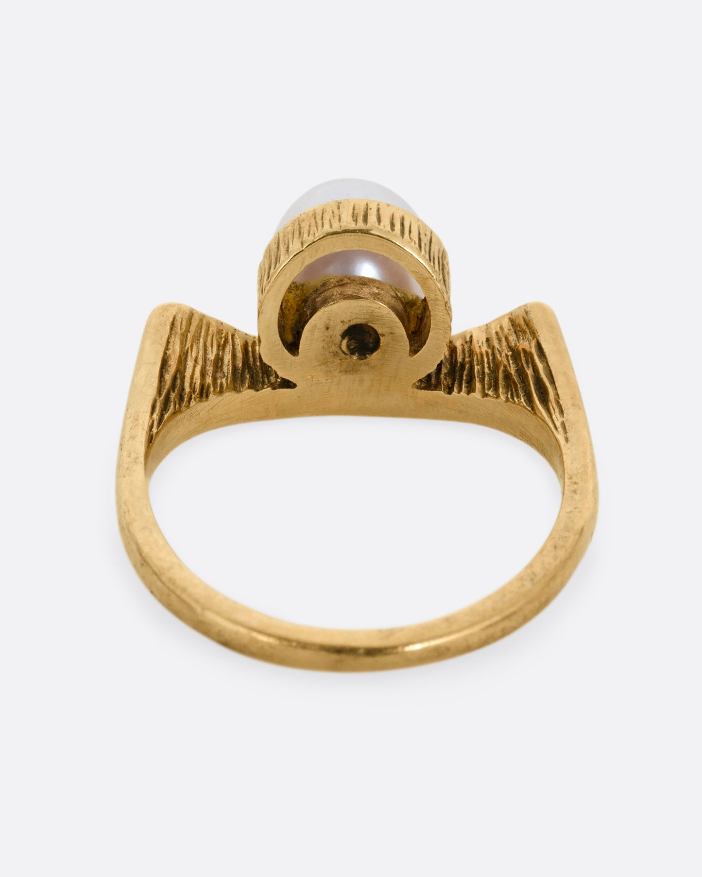 A yellow gold ring with a white pearl shown from the back.