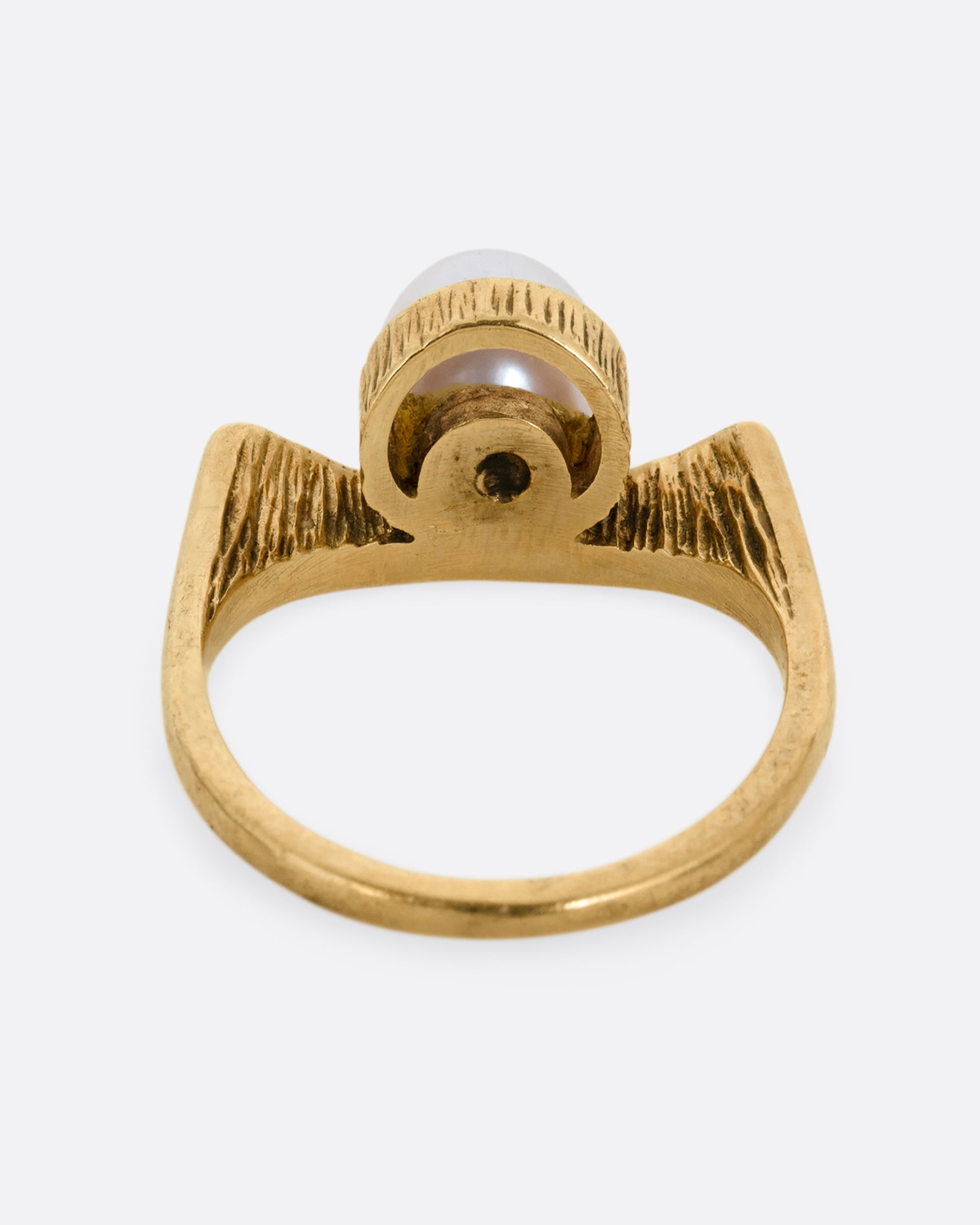 A yellow gold ring with a white pearl shown from the back.
