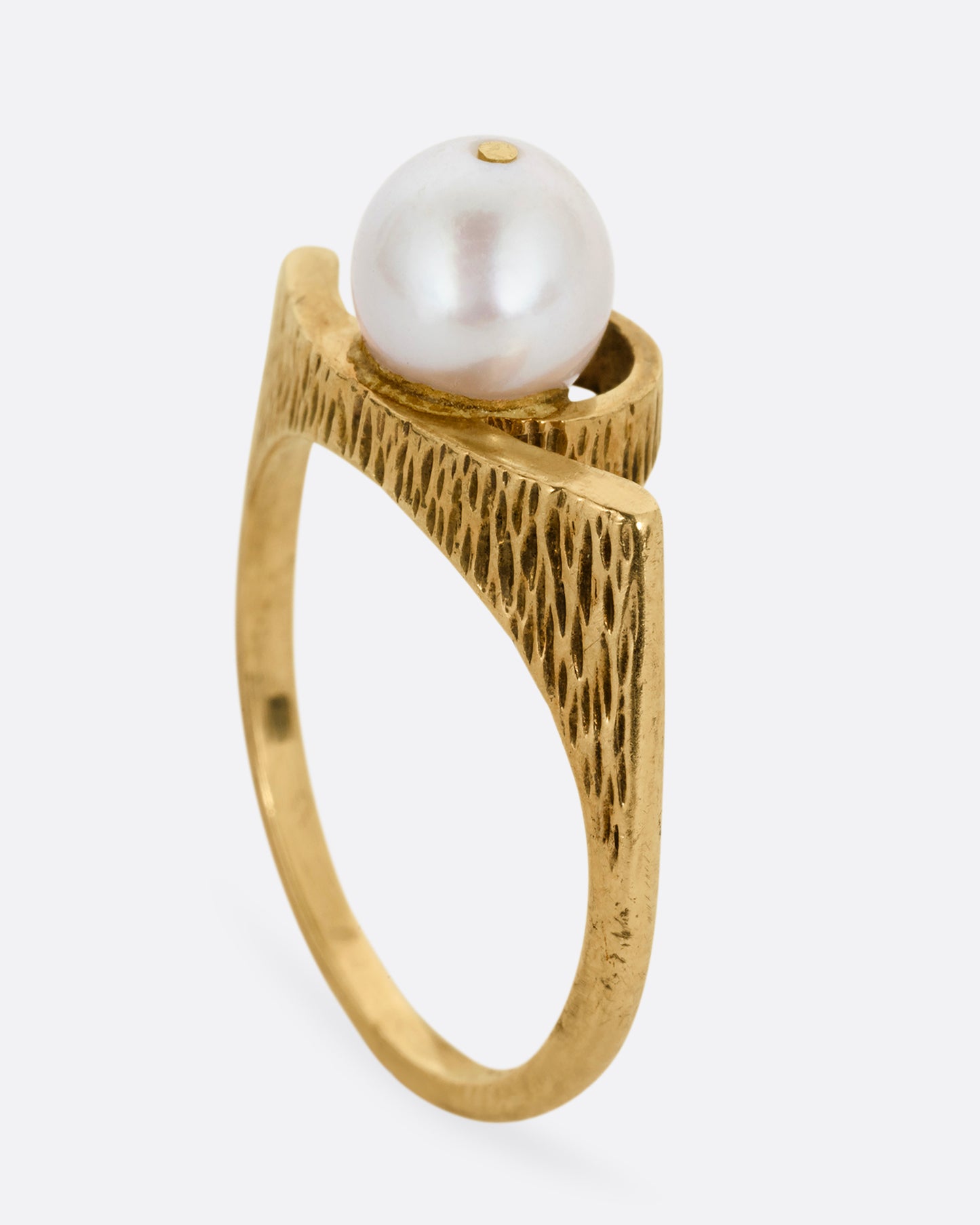 A yellow gold ring with a white pearl shown standing up from the side.