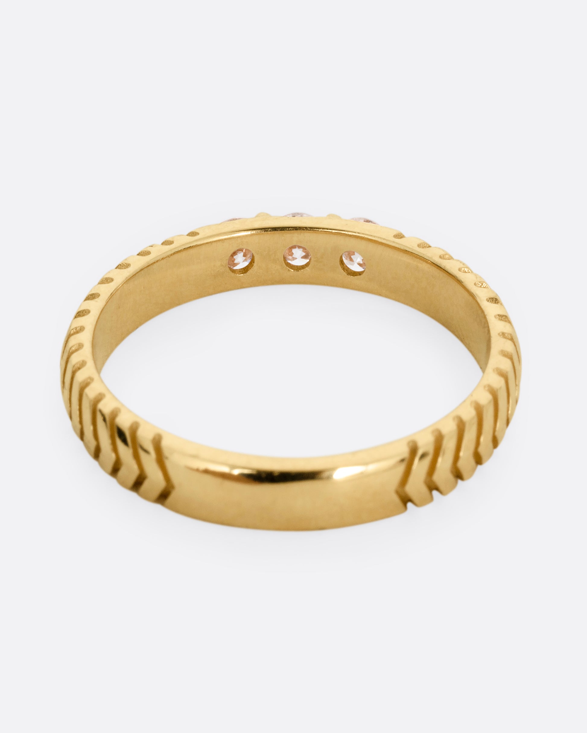 A yellow gold ring with arrow etching and three white diamonds. Shown from the back.