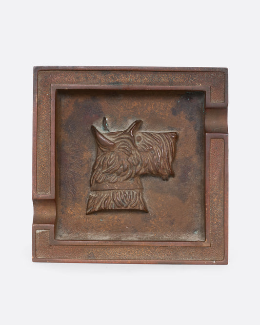 A square brass ashtray with a dunhill Scottie and a cork bottom. Shown from the top.