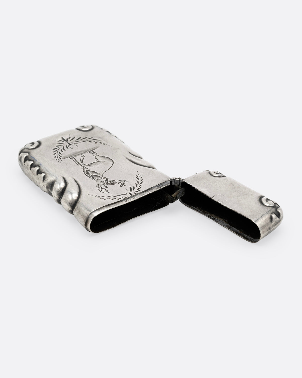 A silver match safe with a deer among scroll work, shown open on its side.