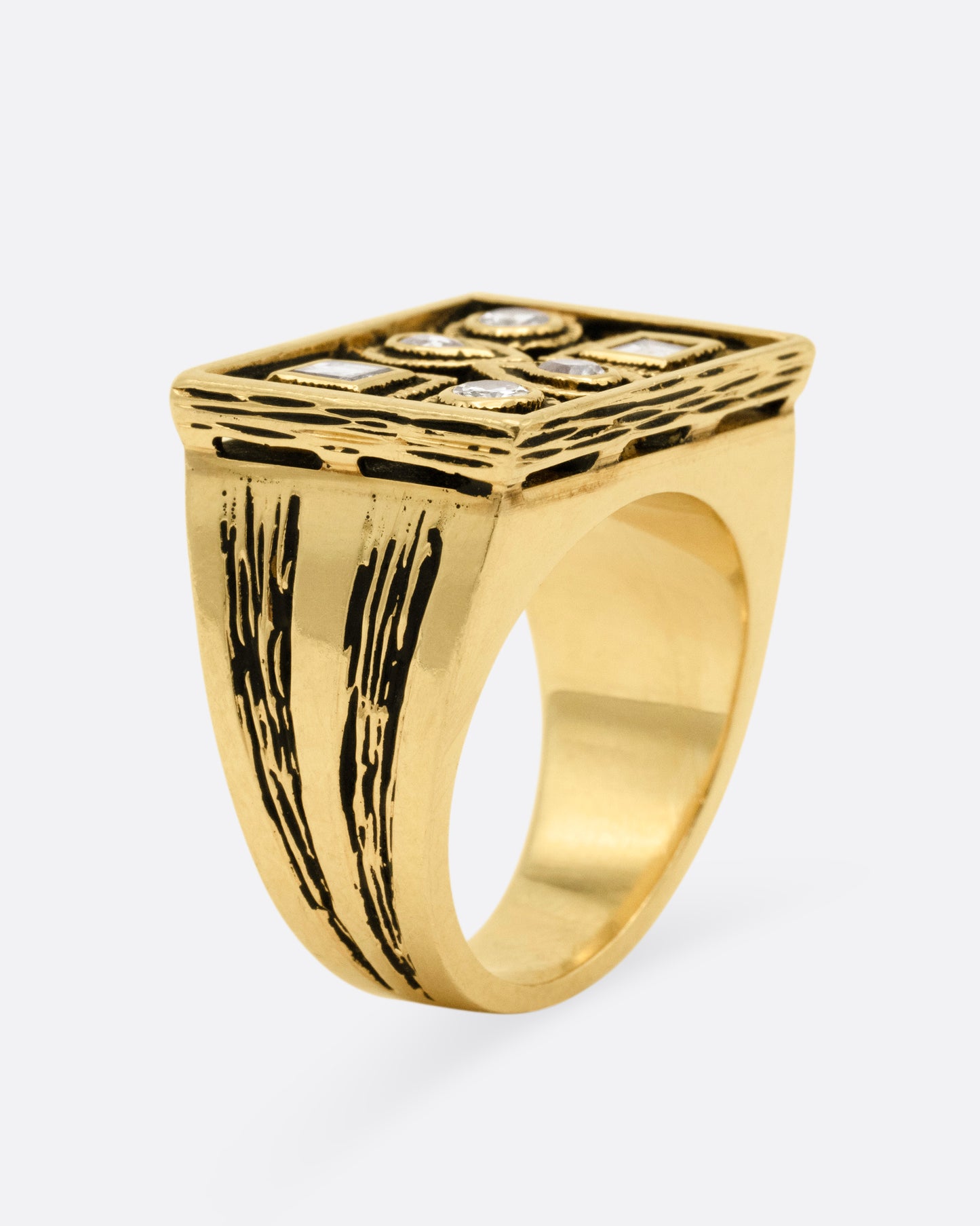 A rectangular yellow gold signet ring with mixed cut diamonds sand textured stone settings and shoulders, shown from the side standing up.