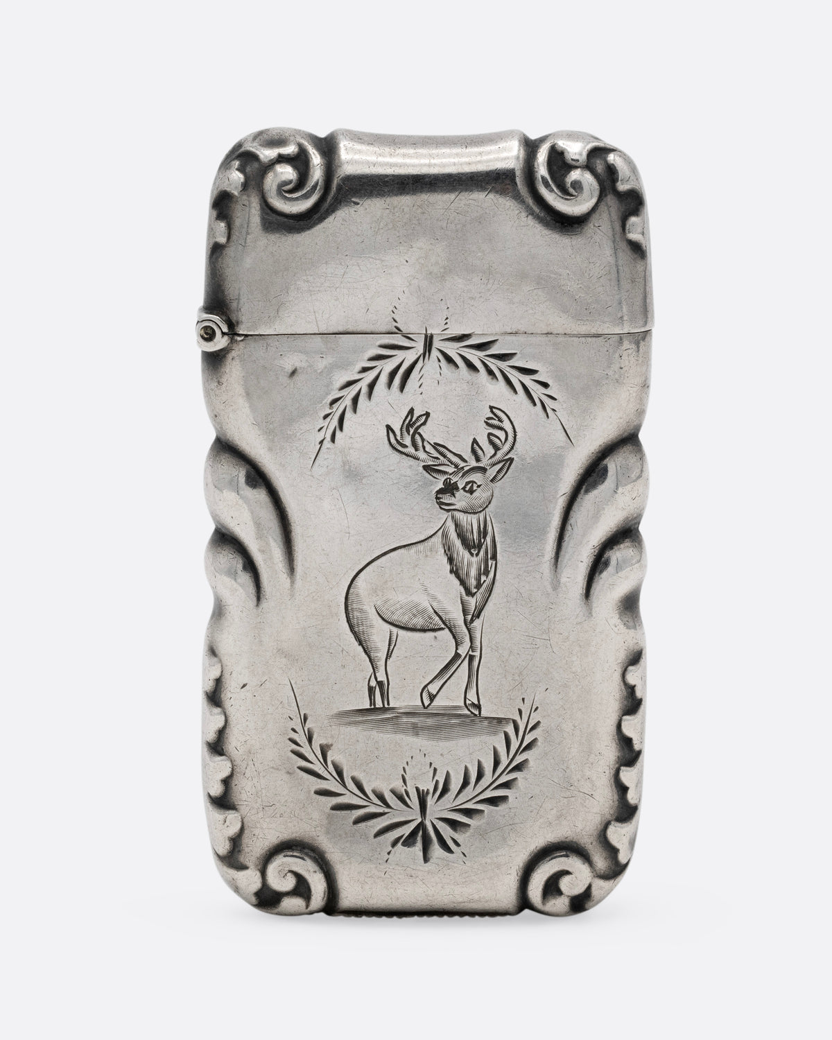A silver match safe with a deer among scroll work, shown from the front.