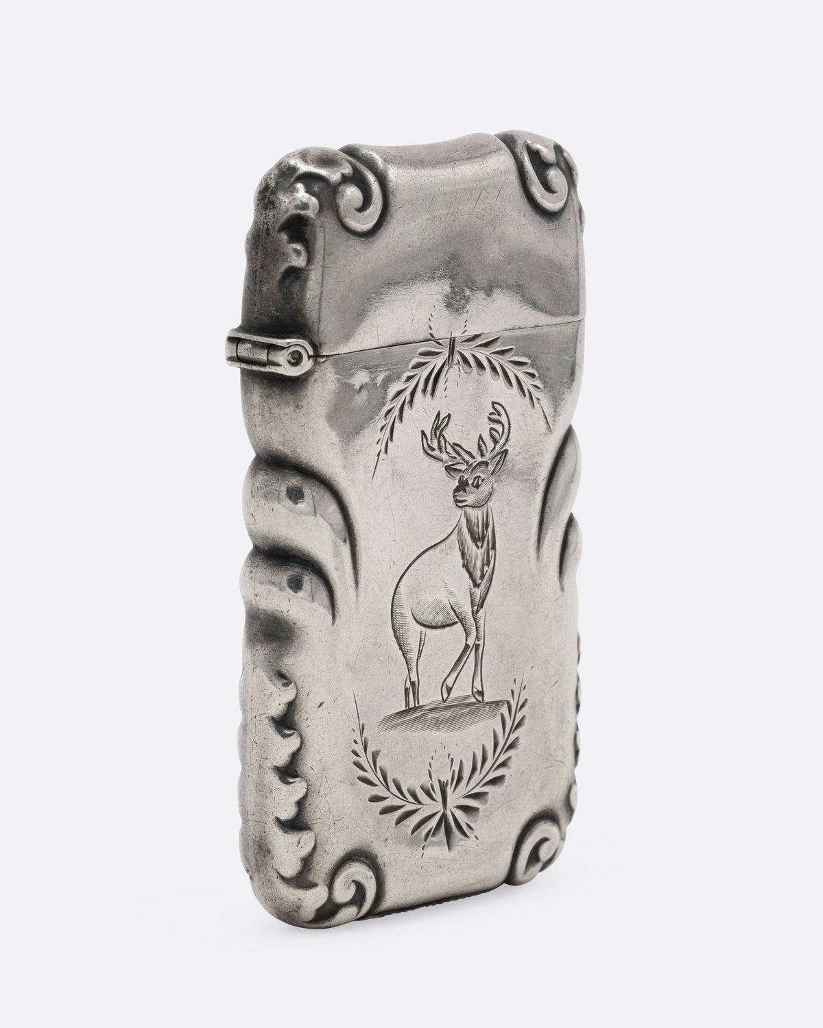 A silver match safe with a deer among scroll work, shown from the side.