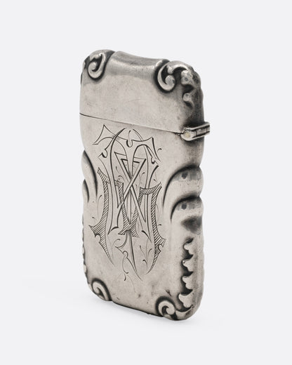 A silver match safe with a deer among scroll work, shown from the side.