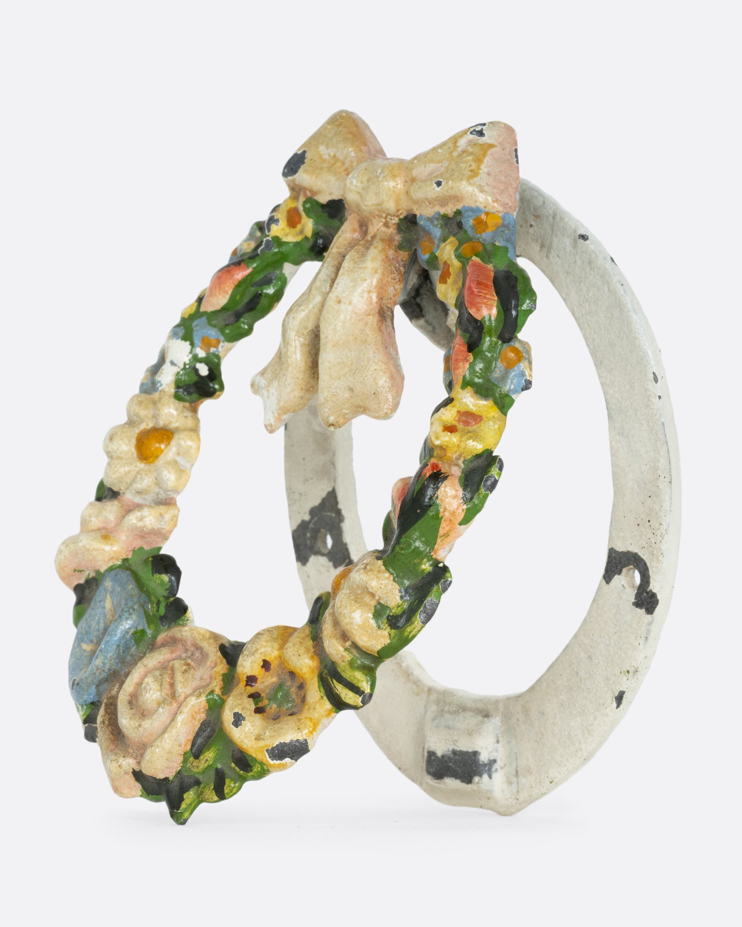 A cast  iron wreath door knocker with a bow and flowers. Shown from the side.
