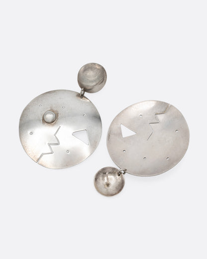 A pair of round drop stud earrings with geometric cutout faces. Shown lying flat.