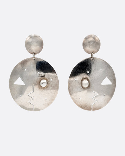 A pair of round drop stud earrings with geometric cutout faces. Shown from the  front.