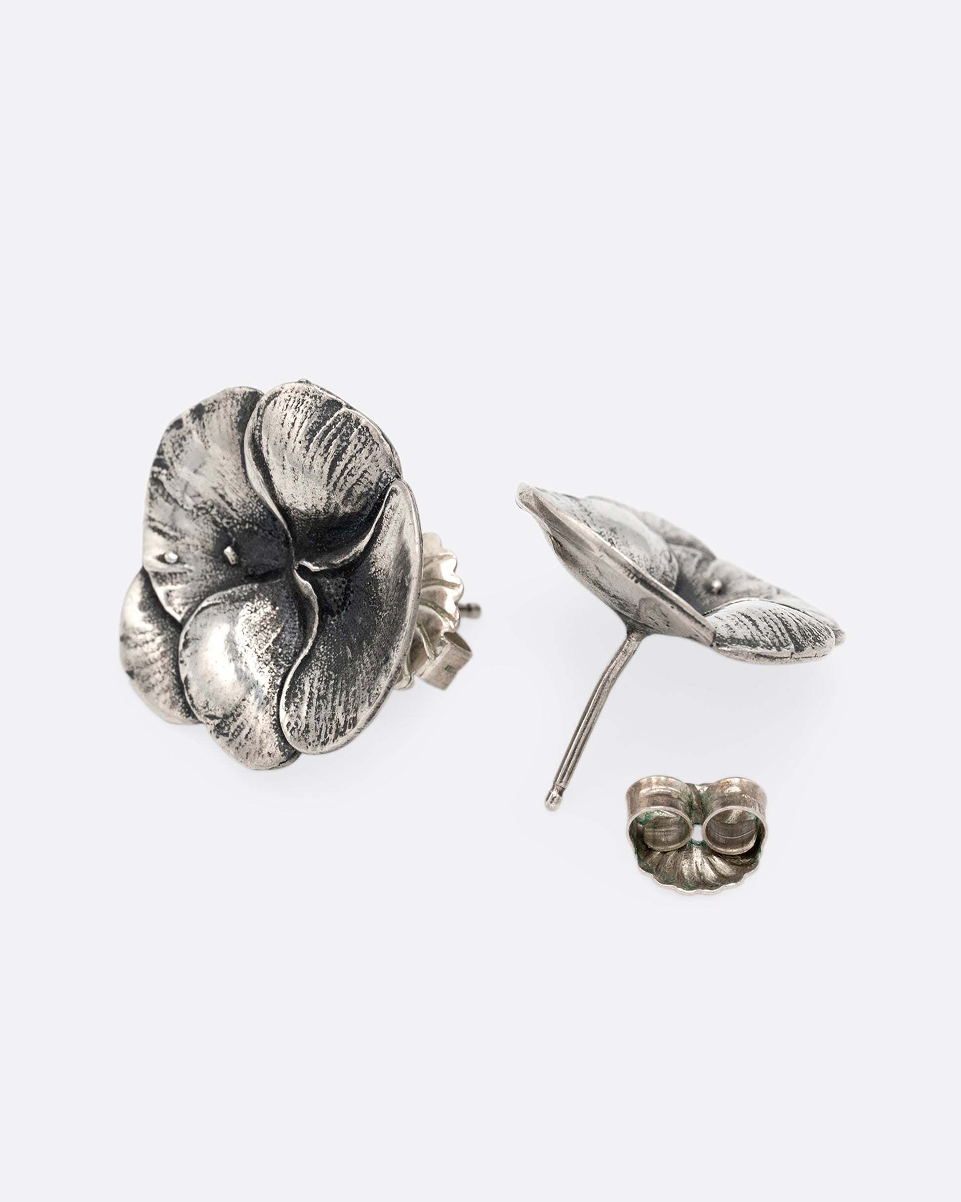 A pair of silver pansy earrings. One is shown from the front, the other from the back.
