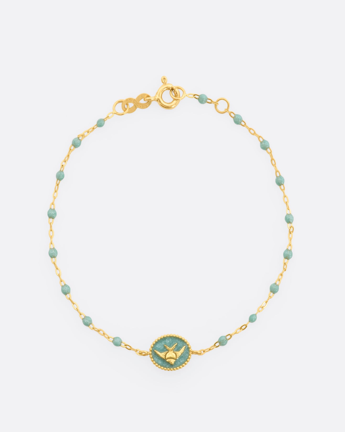 A classic yellow gold Gigi Clozeau bracelet with sparkly iceberg blue resin beads and an oval tag pendant, with a gold angel fish at its center. View of the bracelet from above, closed.