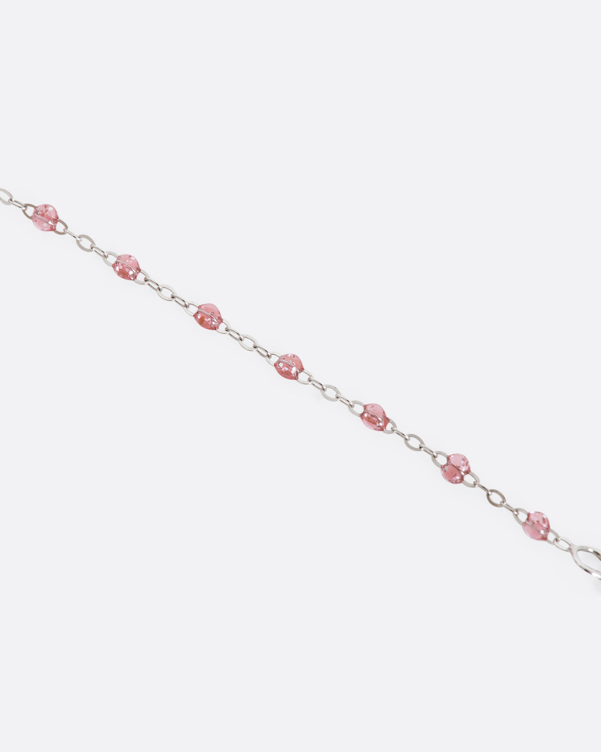 A white gold bracelet with rose pink glitter resin beads and a pave diamond disc and the center. View up close of beads.