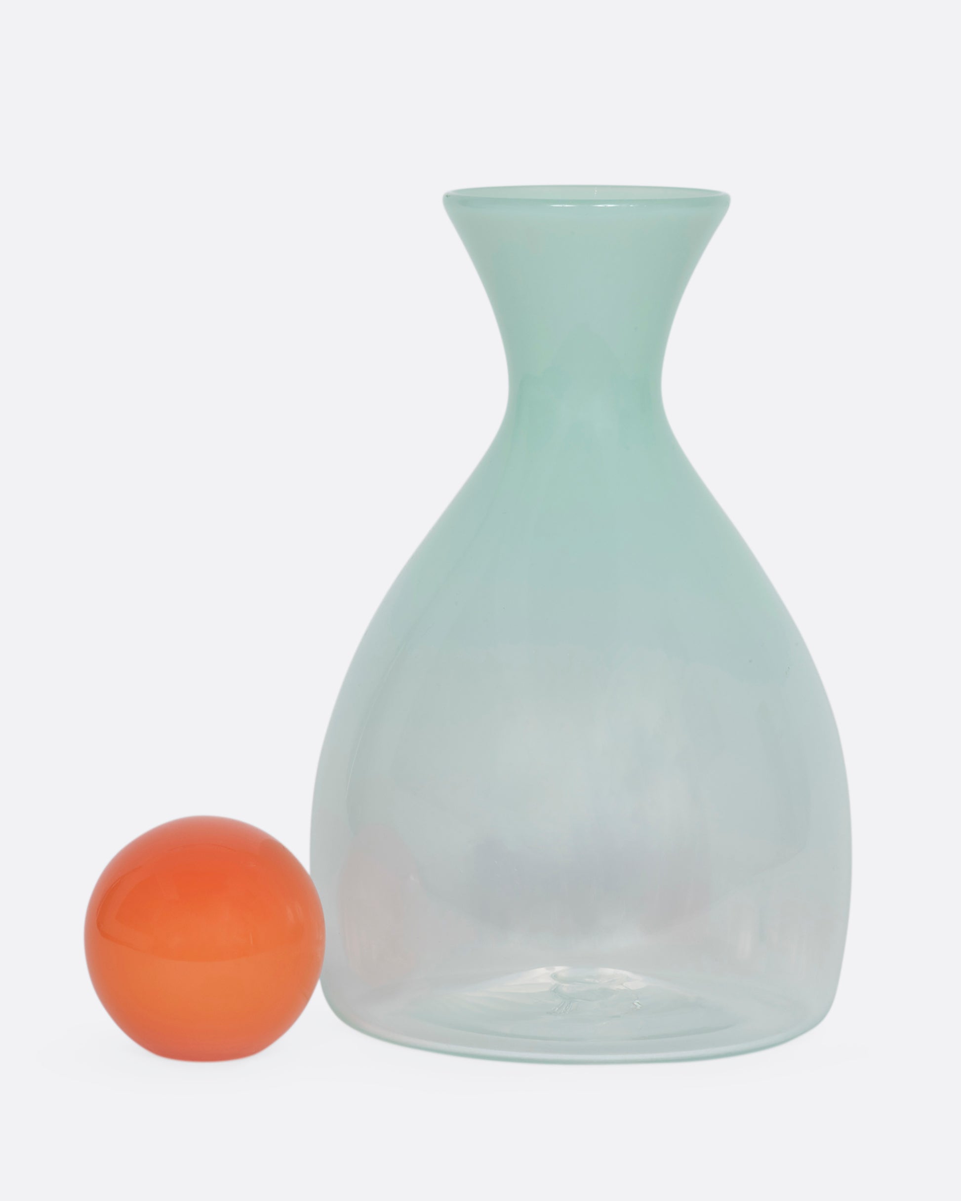 A mint green decanter with an orange sphere stopper. View from the front with the stopper beside.