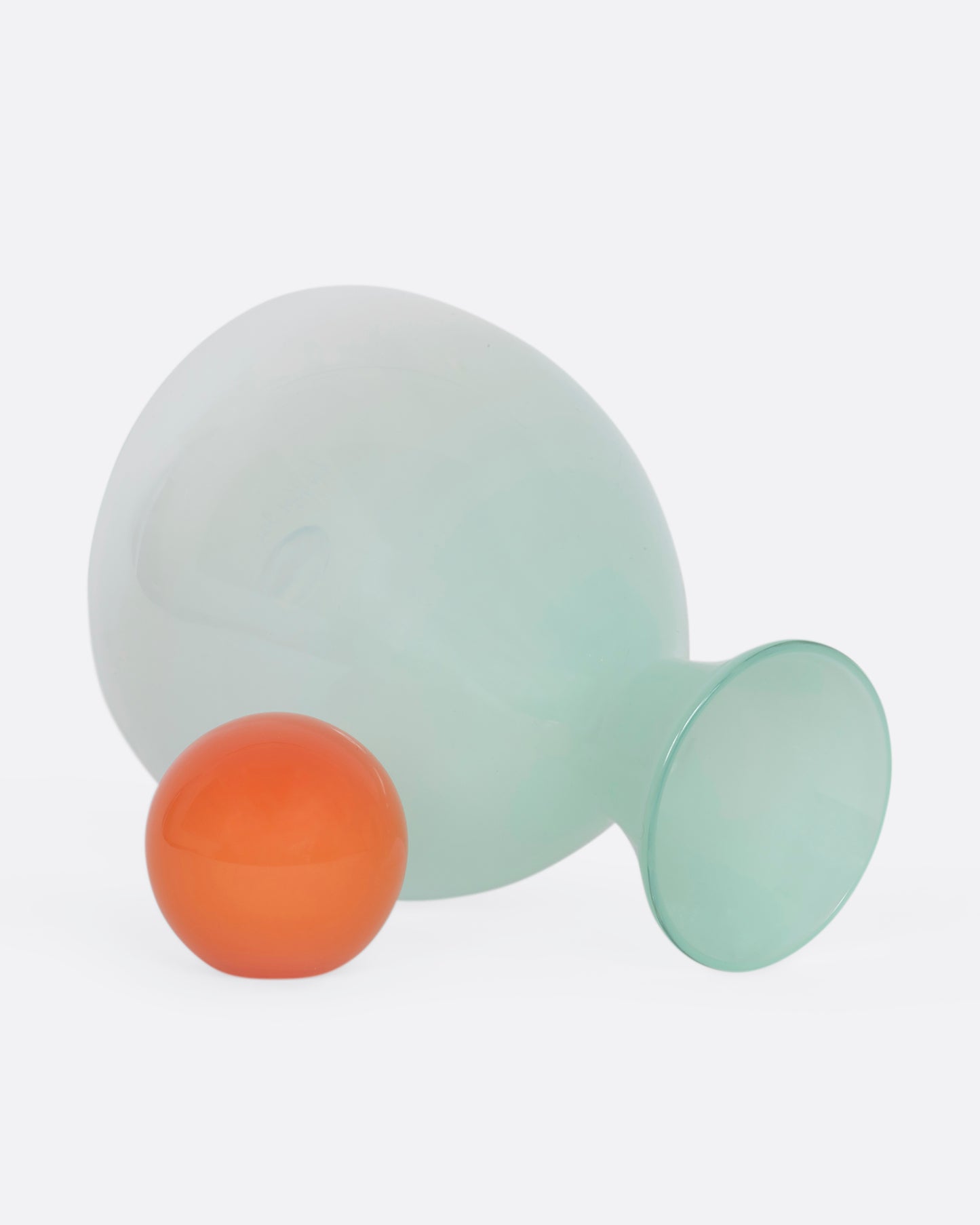 A mint green decanter with an orange sphere stopper. View laying flat with the stopper beside.