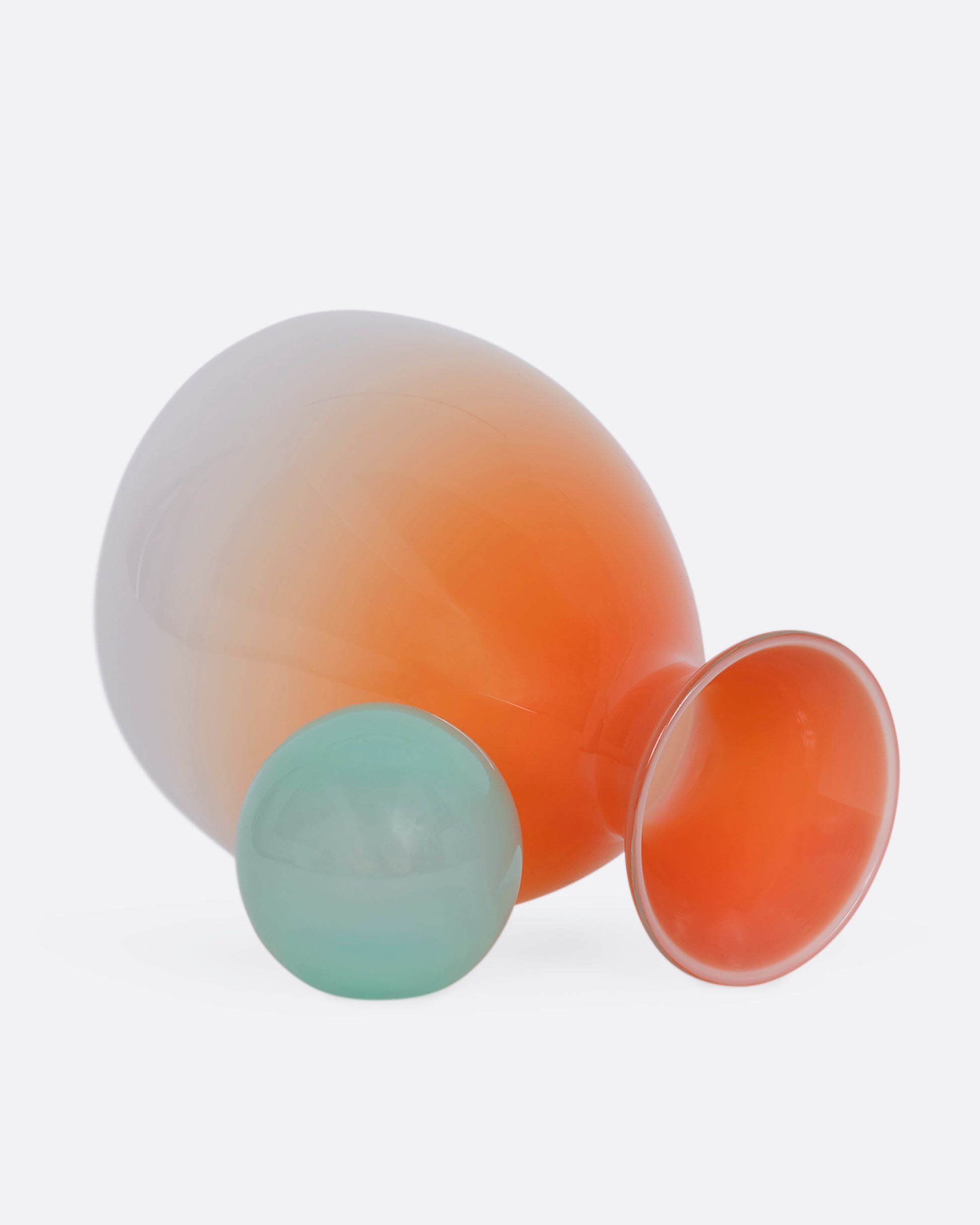 An ombre orange decanter with a mint green sphere stopper. View laying flat with the stopper removed.