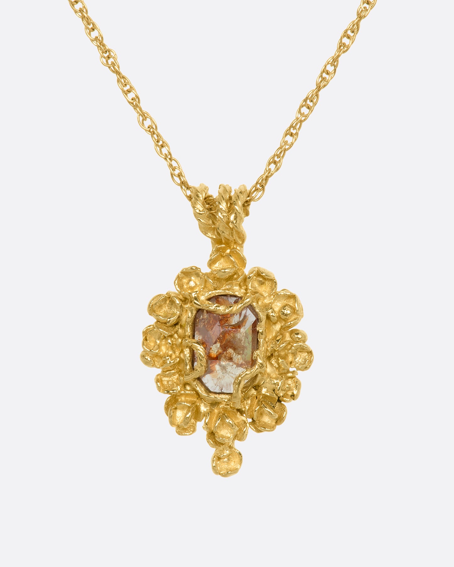 A yellow gold pendant reminiscent of an antique mirror with floral and vine details around an orange rose cut diamond. View from the front.