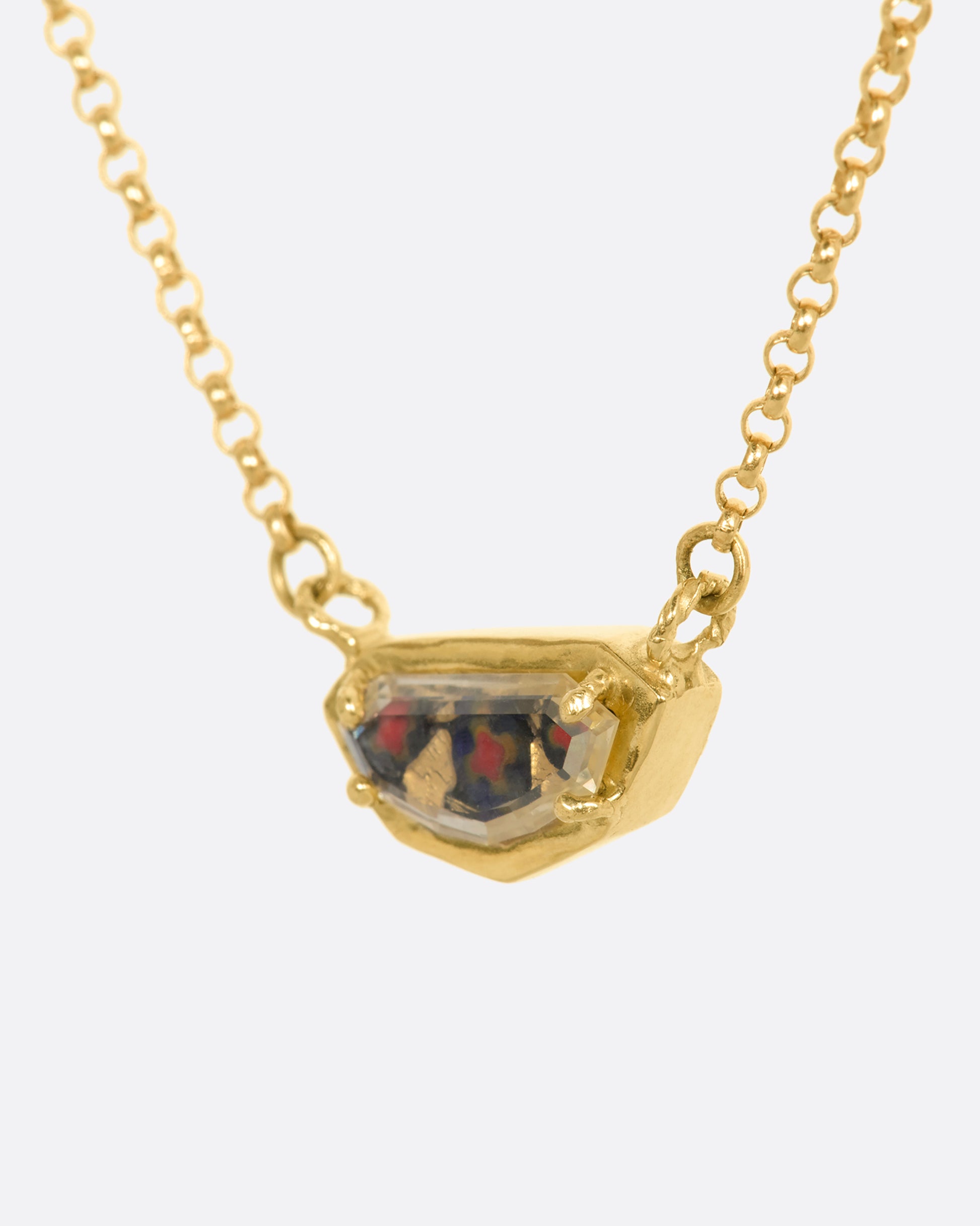 A yellow gold shield shaped necklace with a portrait cut sapphire over micromosaic and goldleaf italian glass and black diamond. View from the side.