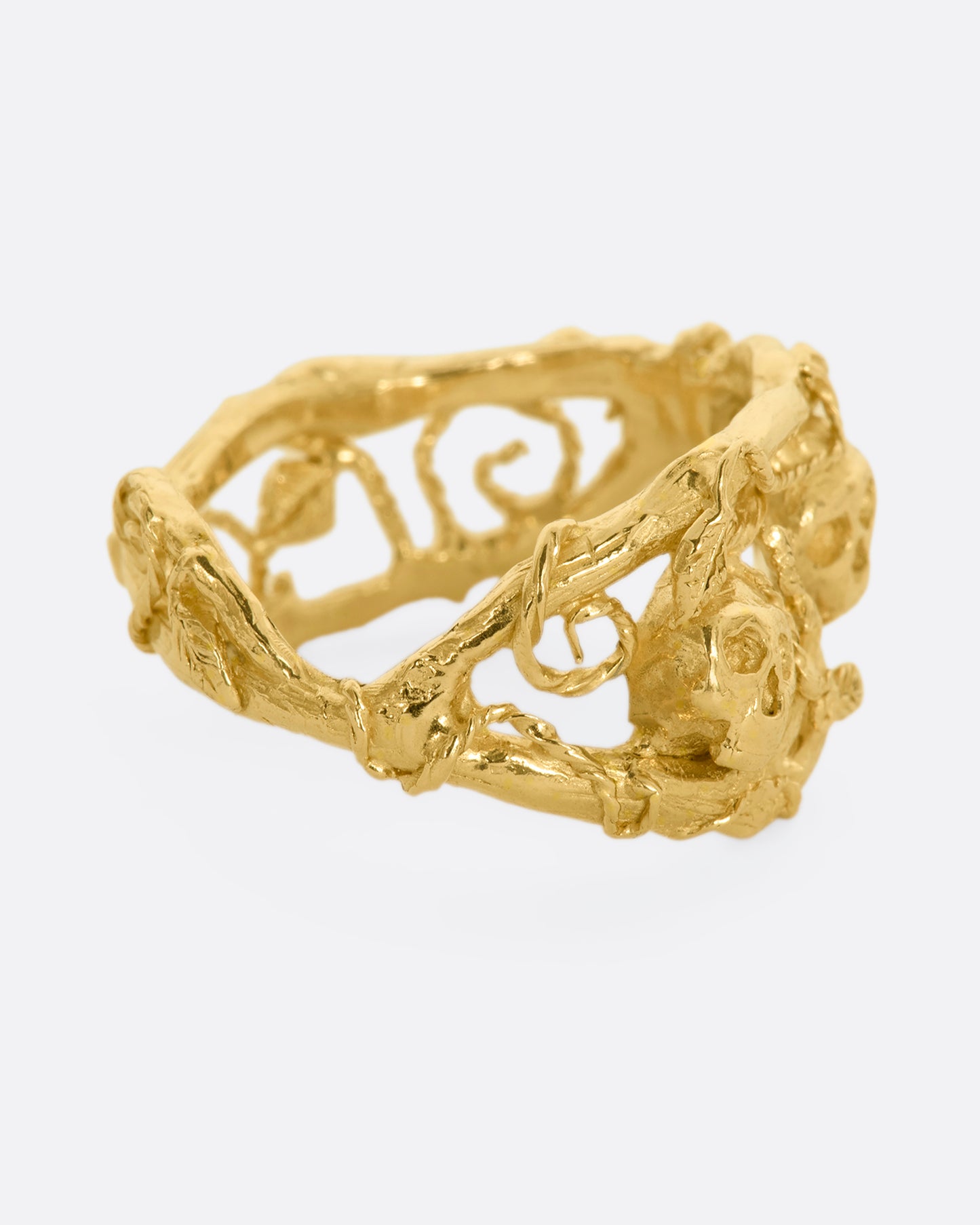 A yellow gold momento mori ring with organic branch and vine motif, featuring two skulls. View from the alternate side.