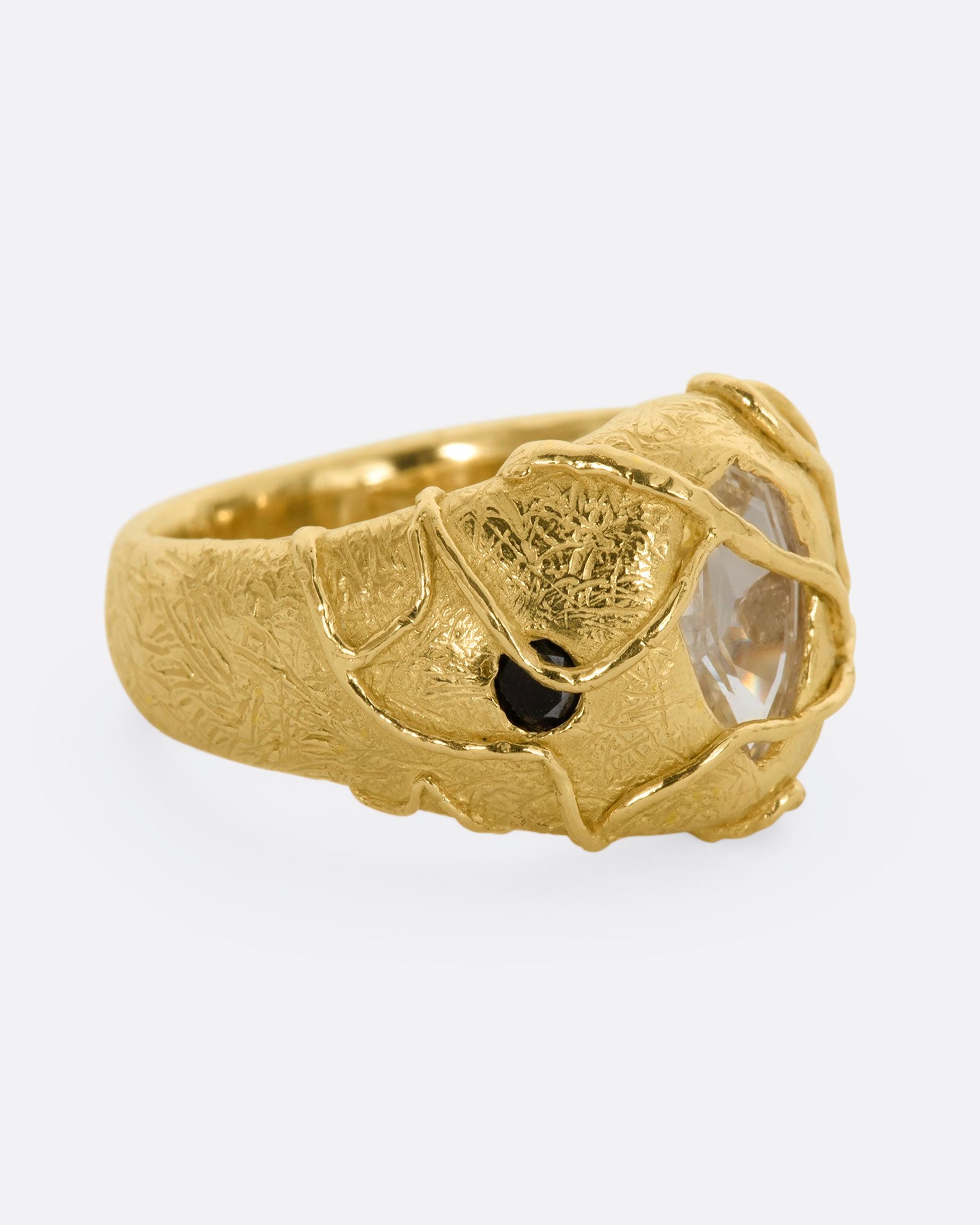 A chunky yellow gold ring with a vine motif that looks like it's grown over the fancy step cut sapphire at the center and the brilliant black diamonds. View from the alternate side.