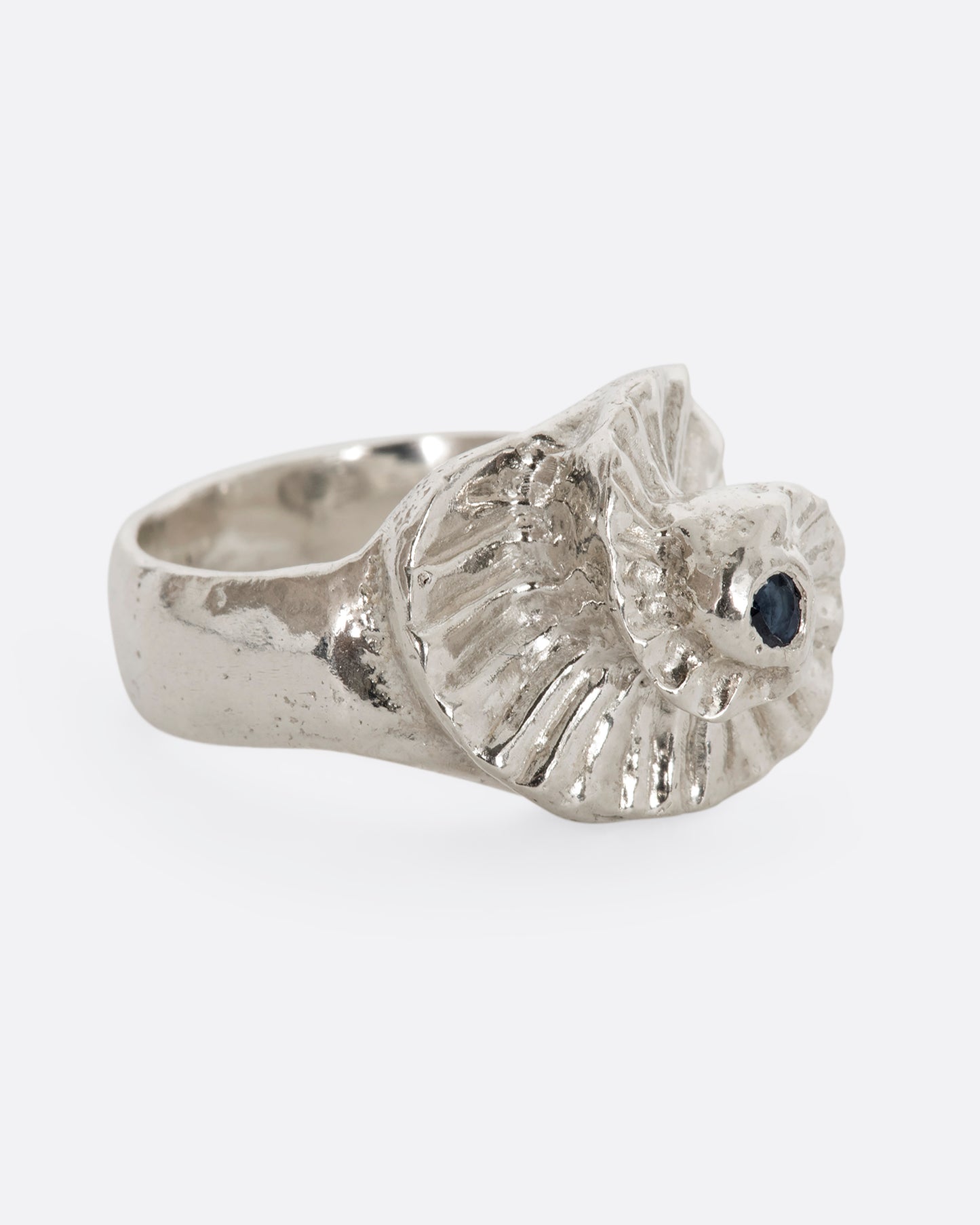 A sterling silver textured spiral ring with a single blue sapphire at the center. View from the alternate side.