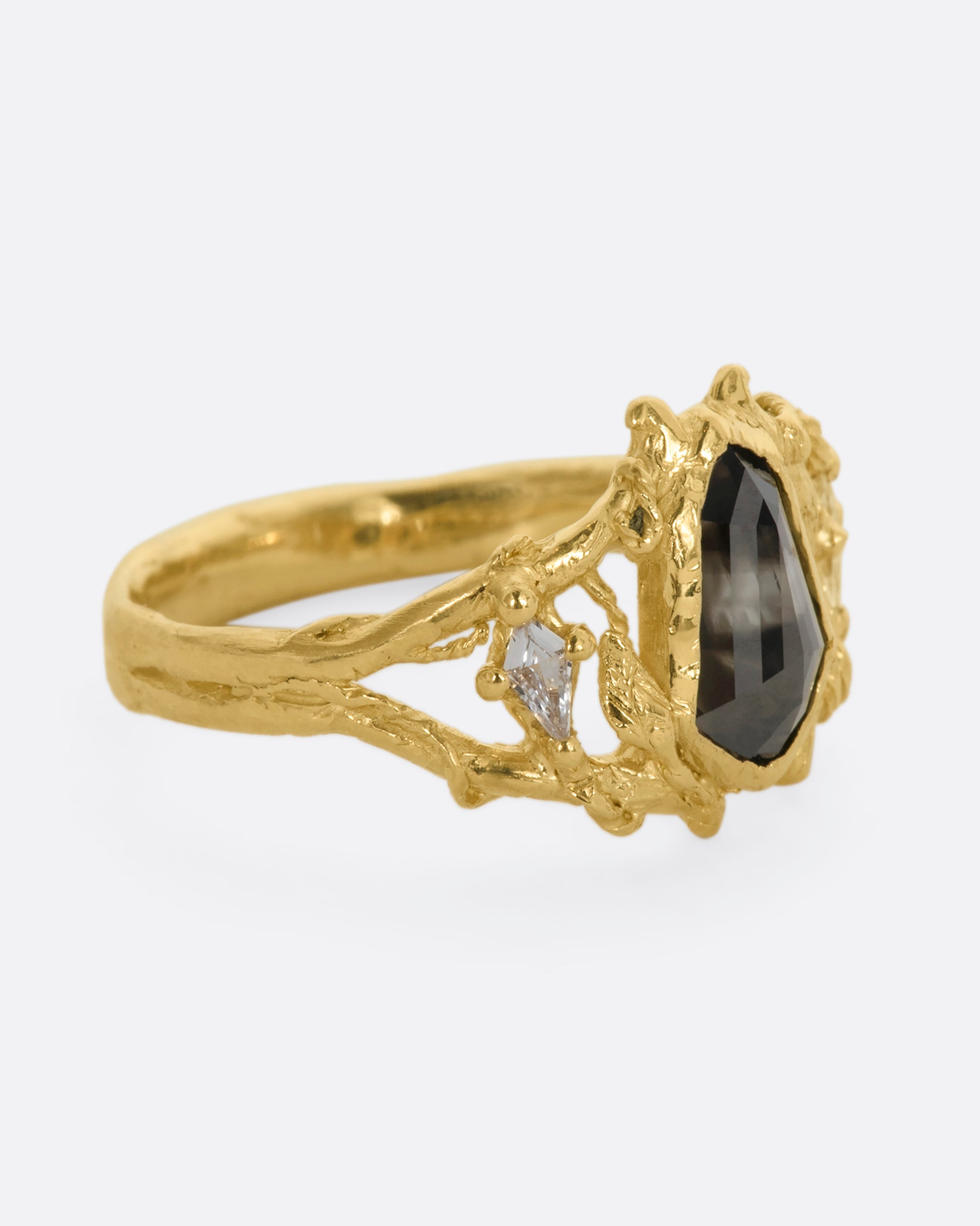 A yellow gold ring with an organic vine motif and a shield double cut black diamond at the center with white kite sapphires on either side. View from the alternate side.