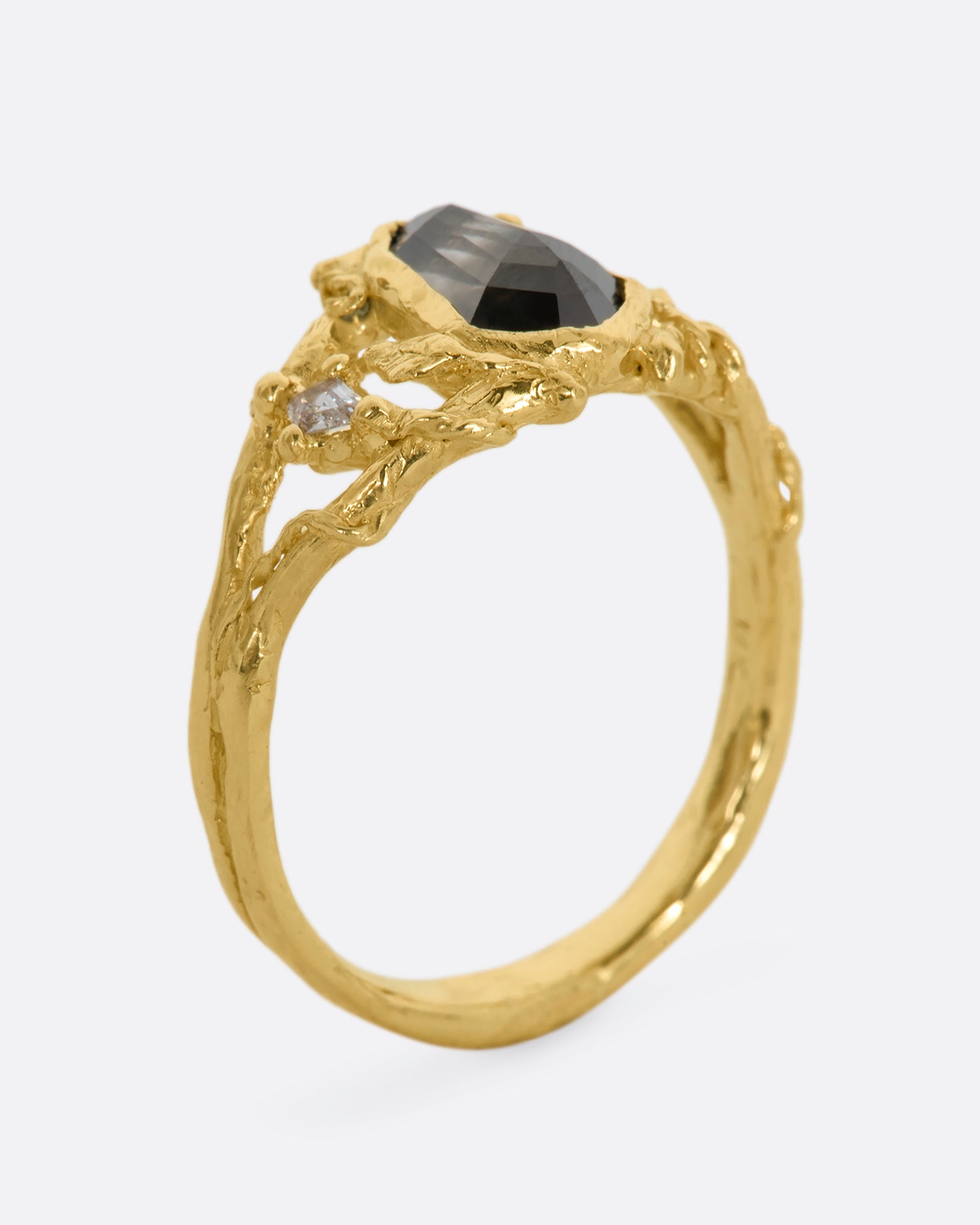 A yellow gold ring with an organic vine motif and a shield double cut black diamond at the center with white kite sapphires on either side. View from the side, standing up.