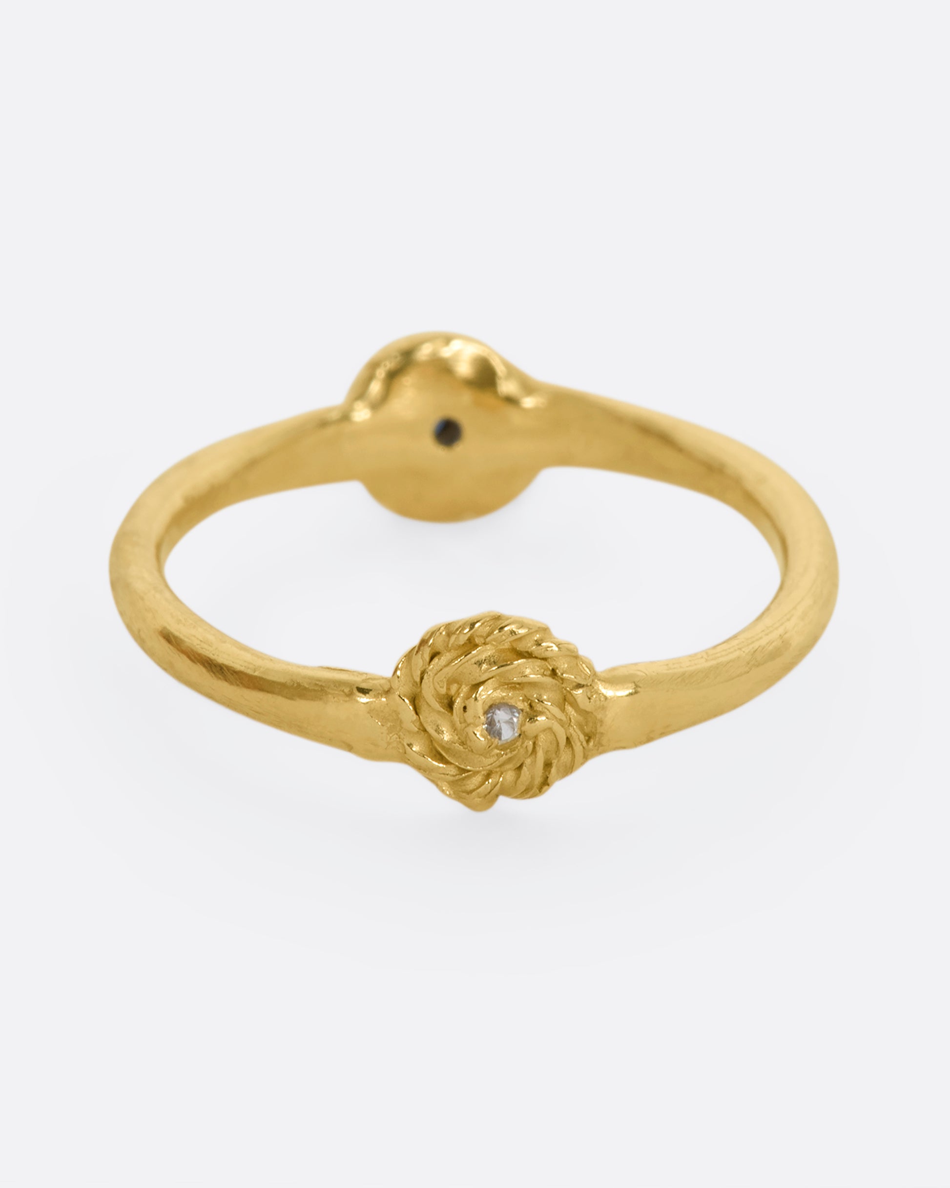 A yellow gold ring with a rosebud motif on either side, one with a white sapphire, the other with a blue sapphire for wear two ways. View from the white sapphire side.