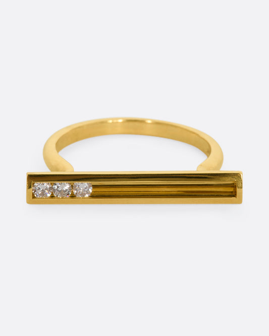 A polished yellow gold ring with a rectangular face that holds three channel set sliding diamonds. View from the front.