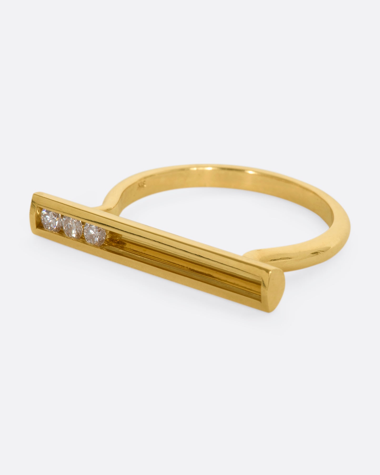 A polished yellow gold ring with a rectangular face that holds three channel set sliding diamonds. View from the side.