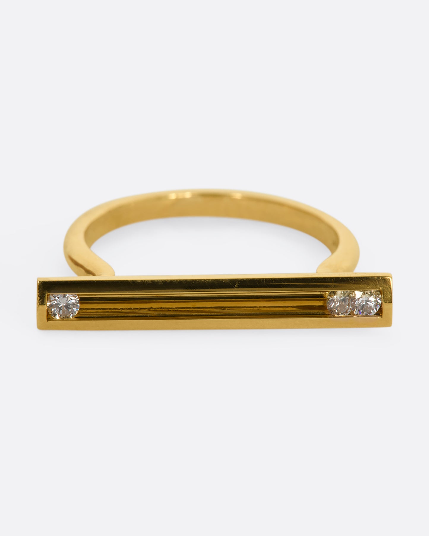 A polished yellow gold ring with a rectangular face that holds three channel set sliding diamonds. View from the front.