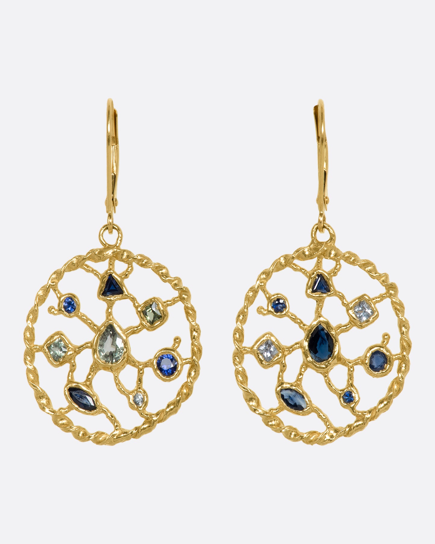 A pair of yellow gold drop earrings with blue and green sapphires sitting on a circular web. View from the front.