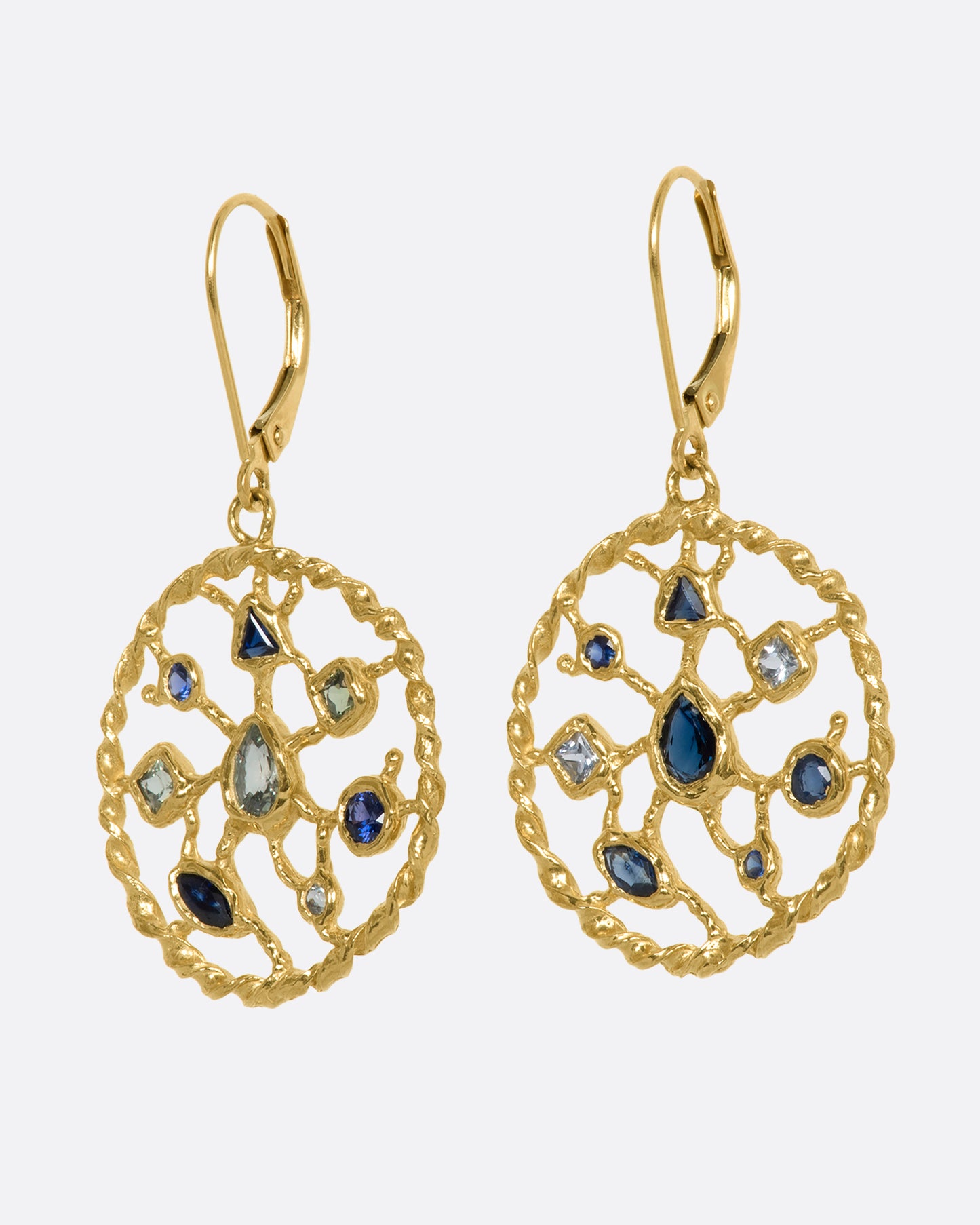 A pair of yellow gold drop earrings with blue and green sapphires sitting on a circular web. View from the side.