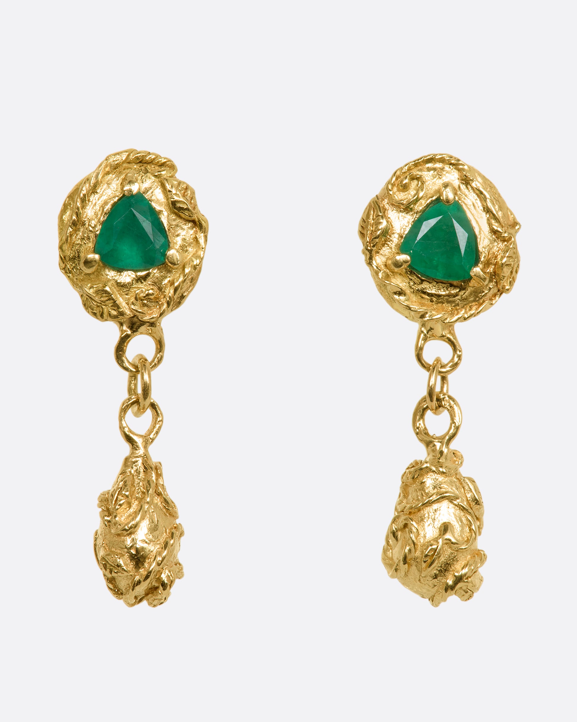 A pair of yellow gold drop earrings with vine motif and a trillion cut emerald on each. View from the front.