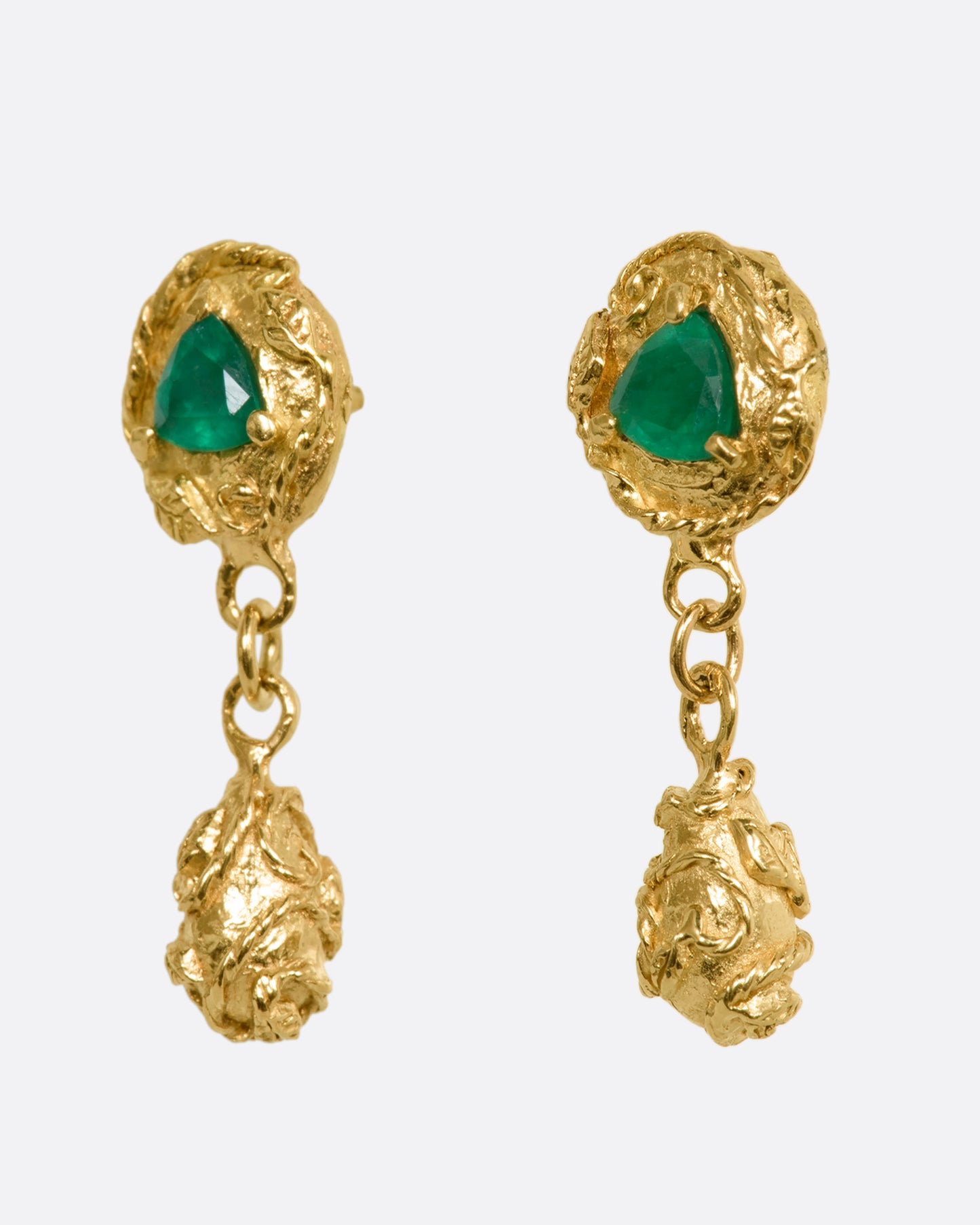 A pair of yellow gold drop earrings with vine motif and a trillion cut emerald on each. View from the side.