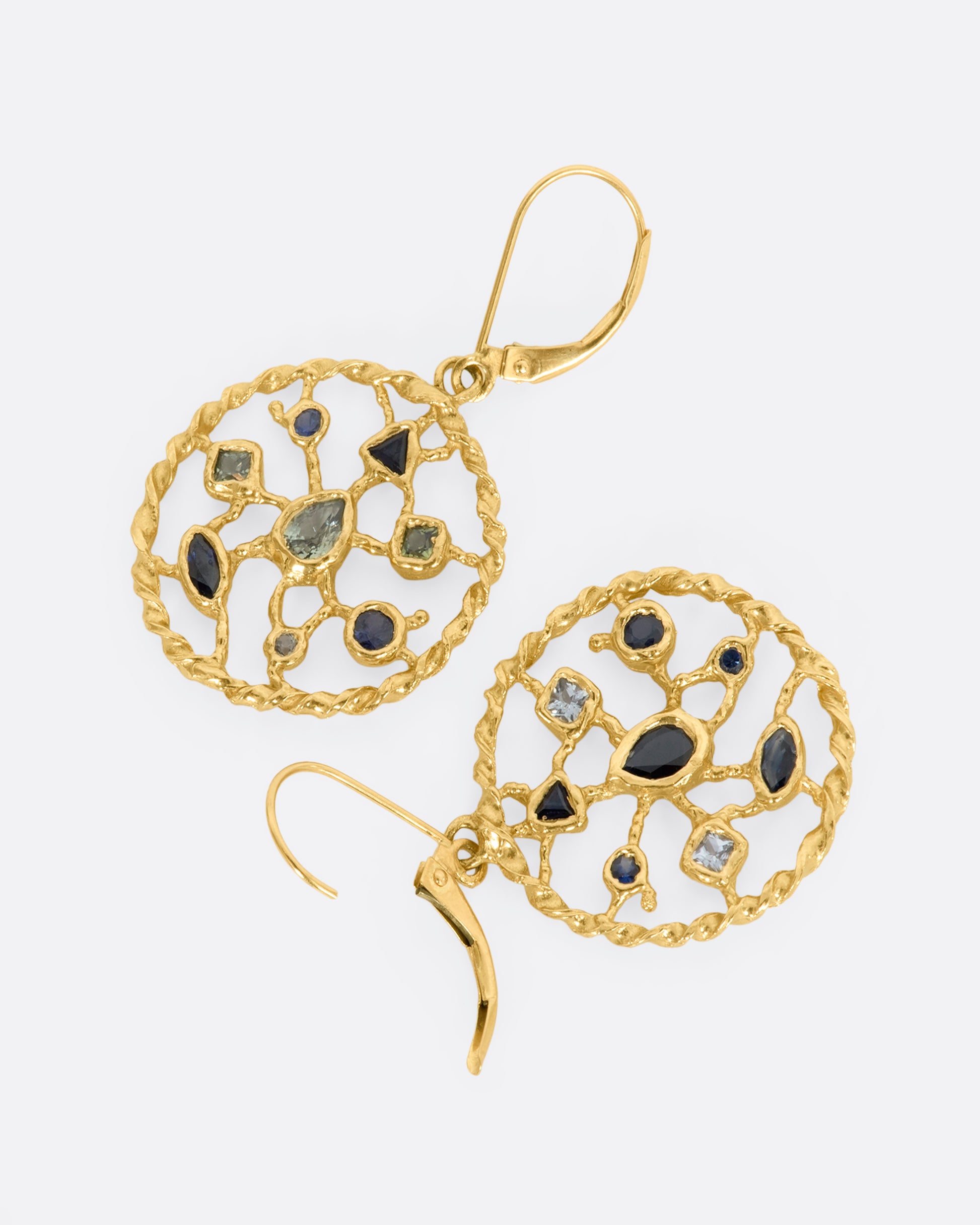 A pair of yellow gold drop earrings with blue and green sapphires sitting on a circular web. View laying flat showing the lever closure.