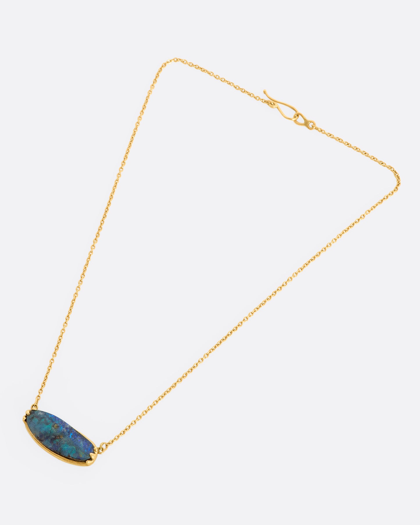 A blue Australian opal sits in a yellow gold east west claw setting and hangs from a yellow gold chain. View from above of the entire necklace.