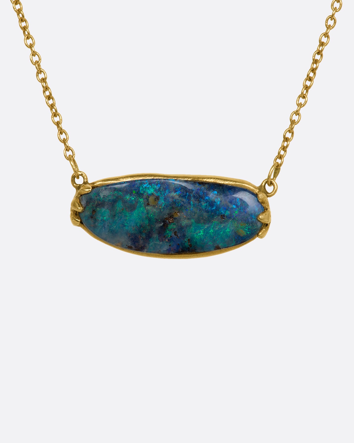 A blue Australian opal sits in a yellow gold east west claw setting and hangs from a yellow gold chain. View up close from the front.