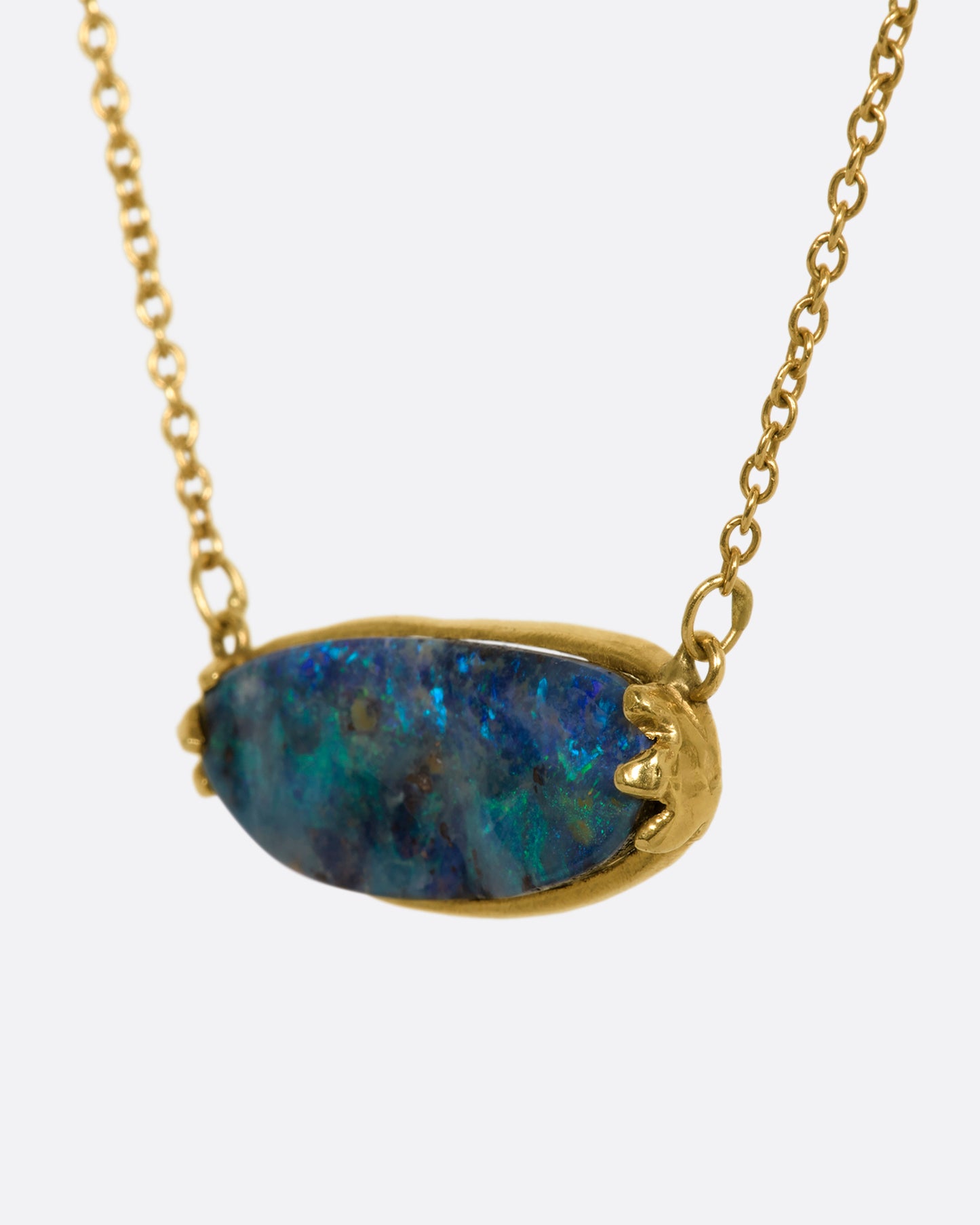 A blue Australian opal sits in a yellow gold east west claw setting and hangs from a yellow gold chain. View up close from the side.