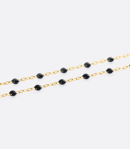 A close up view of a yellow gold cable chain bracelet with black resin droplets. 