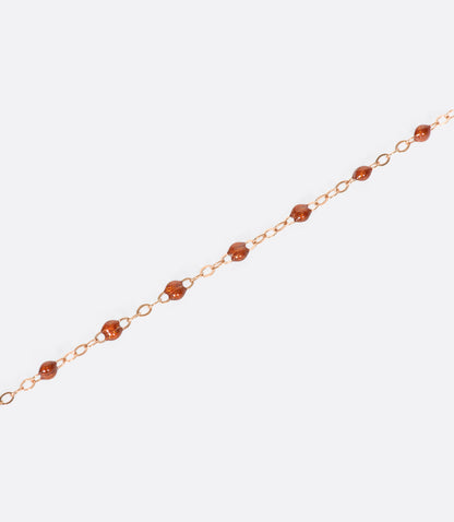 A close up view of a yellow gold cable chain bracelet with rusty red resin droplets. 