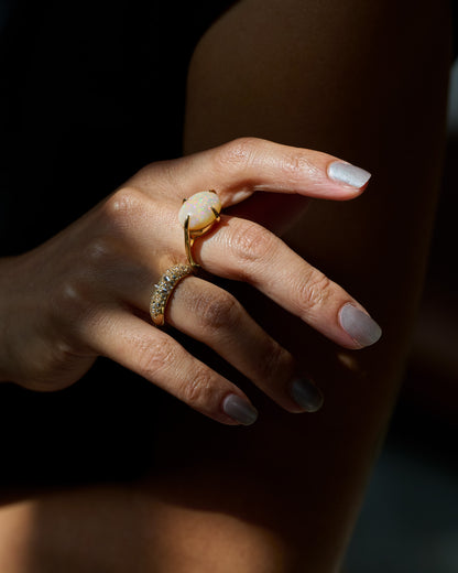 A yellow gold ring with a prong set opal, shown on a person's hand, with a diamond band.