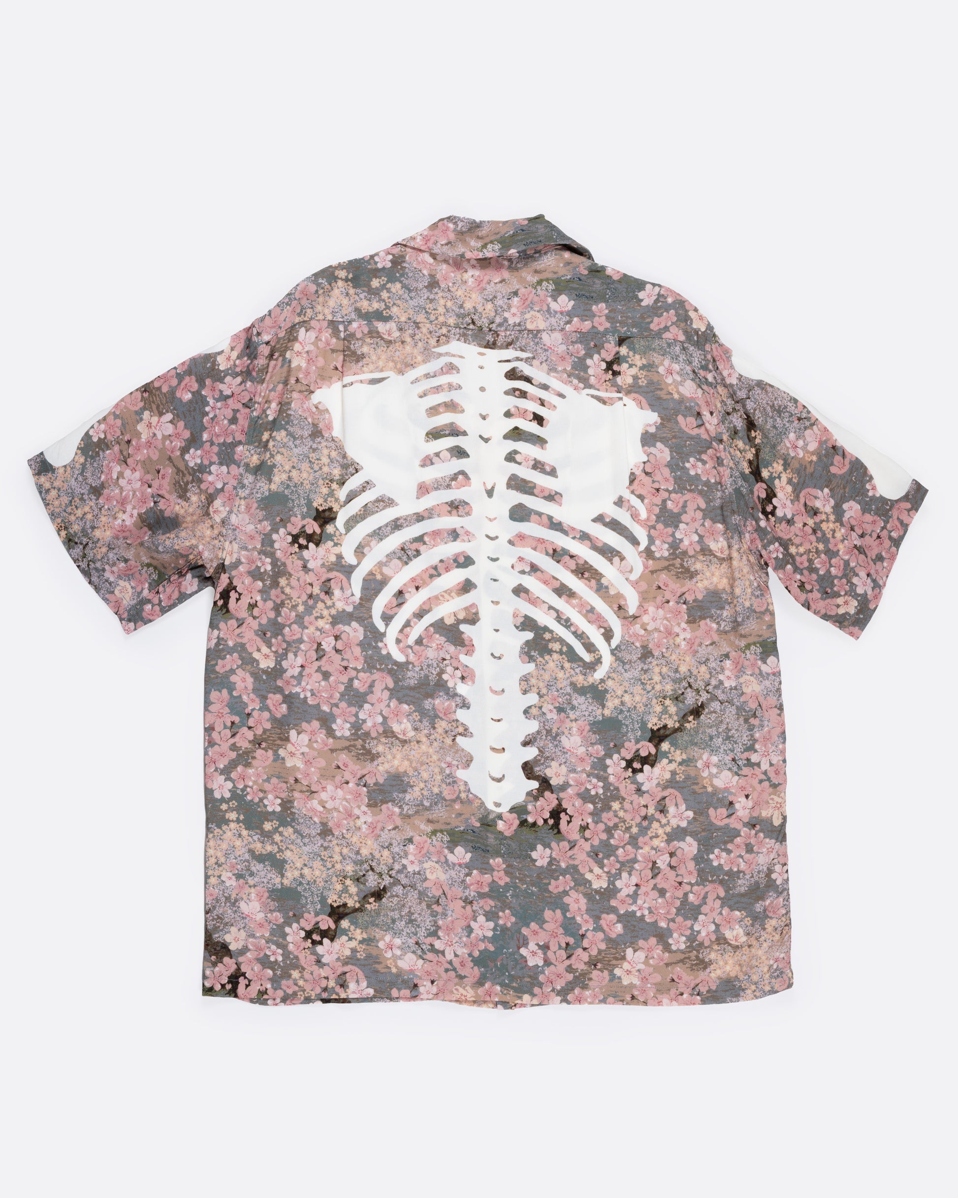 A button front short sleeve shirt with a cherry blossom print punctuated by Kapital’s skeleton motif, shown from the back.
