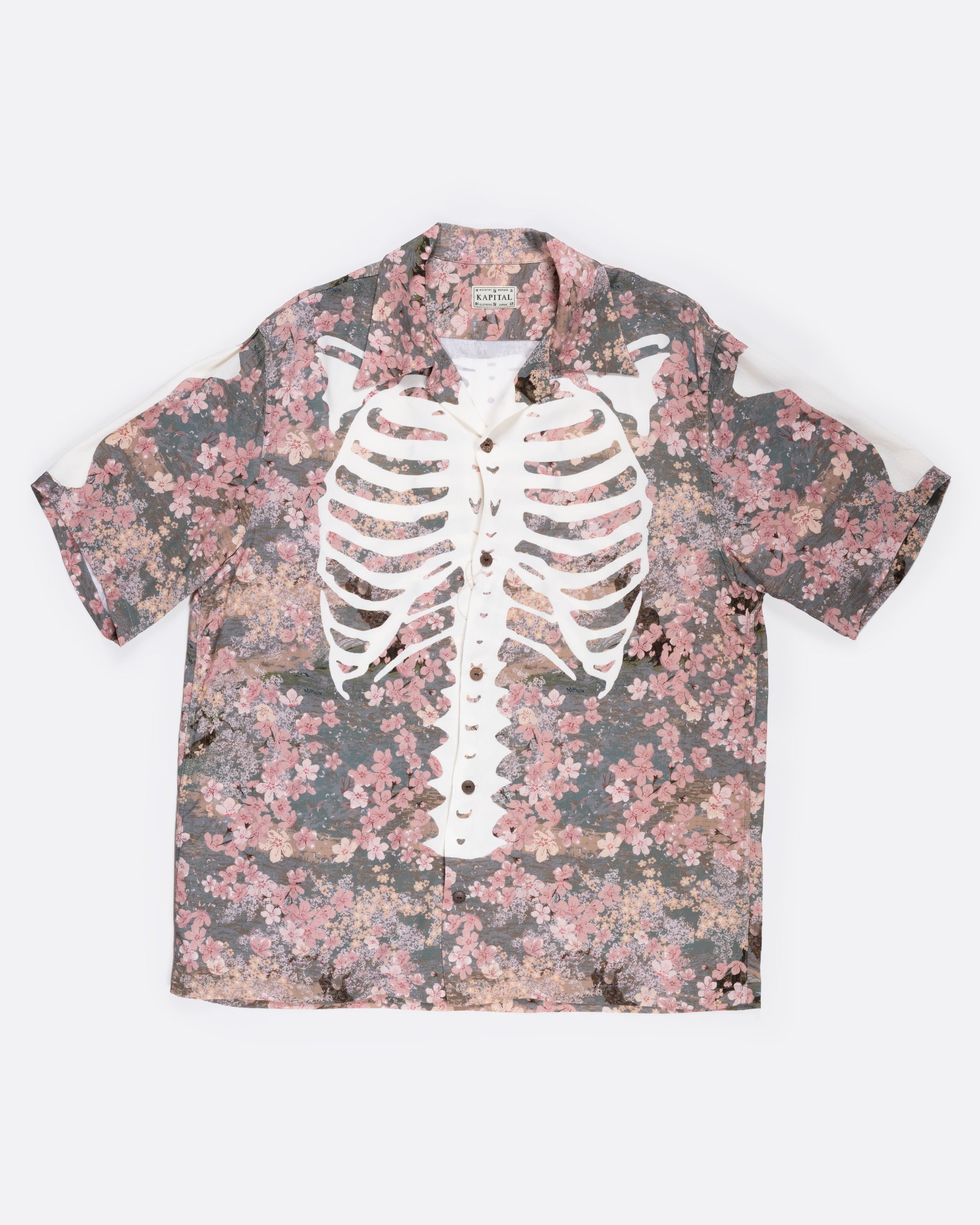 A button front short sleeve shirt with a cherry blossom print punctuated by Kapital’s skeleton motif, shown from the front.