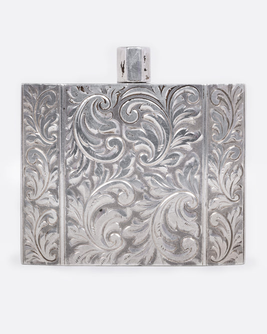 A silver perfume bottle with winding botanical etchings and a slim square silhouette, shown from the front.