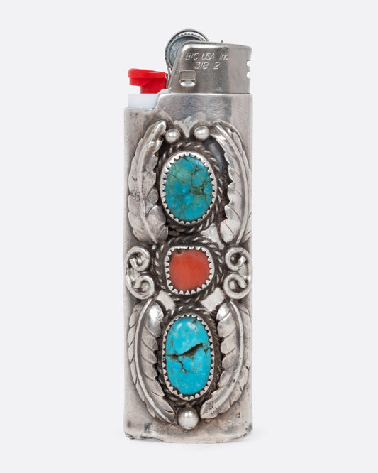 A silver lighter cover with a red stone bookended by two turquoise stones and botanical silver detailing. Shown from the side with a lighter in it.