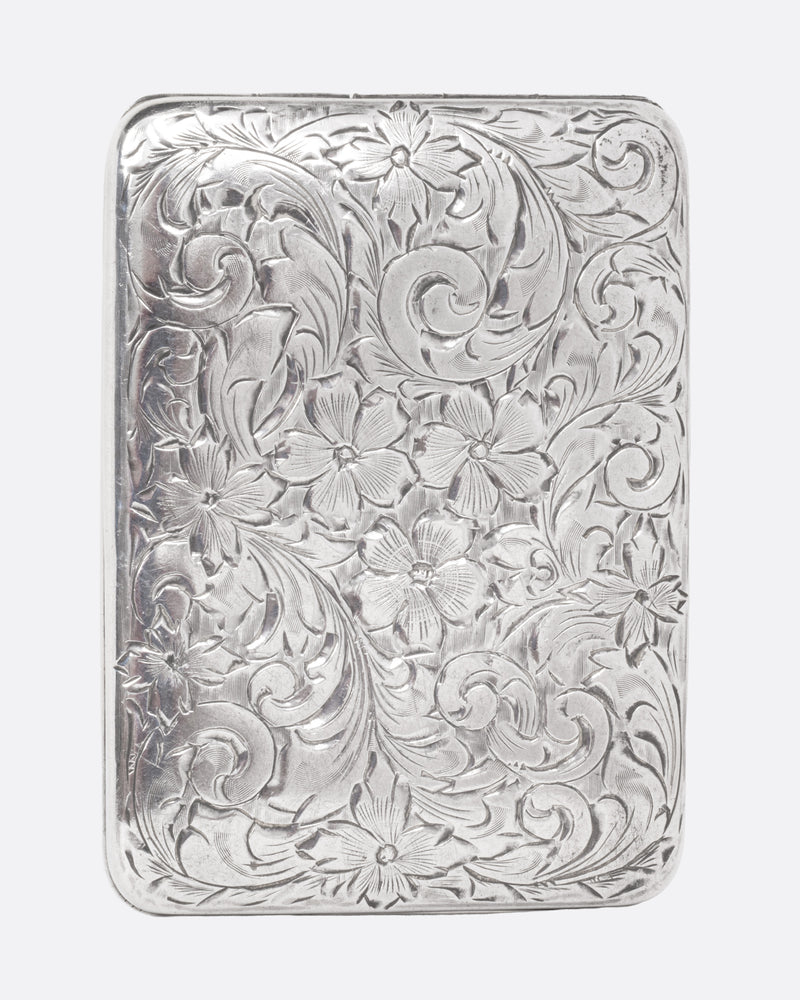 A rectangular silver cigarette box with a hinged top and swirling botanical motif, shown from the front. 