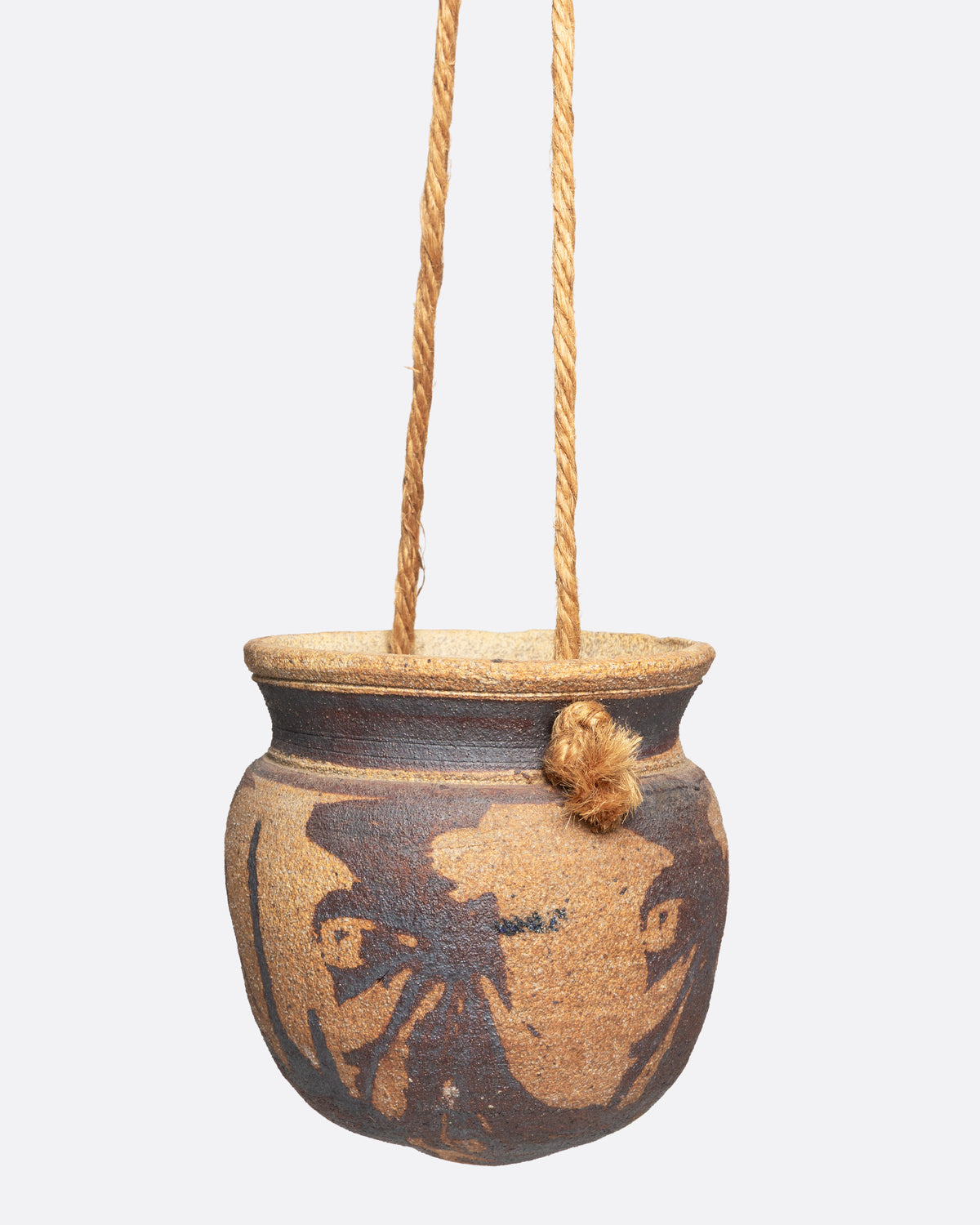 A ceramic pot with an abstract tan and brown pattern and cords for hanging, shown from the side.